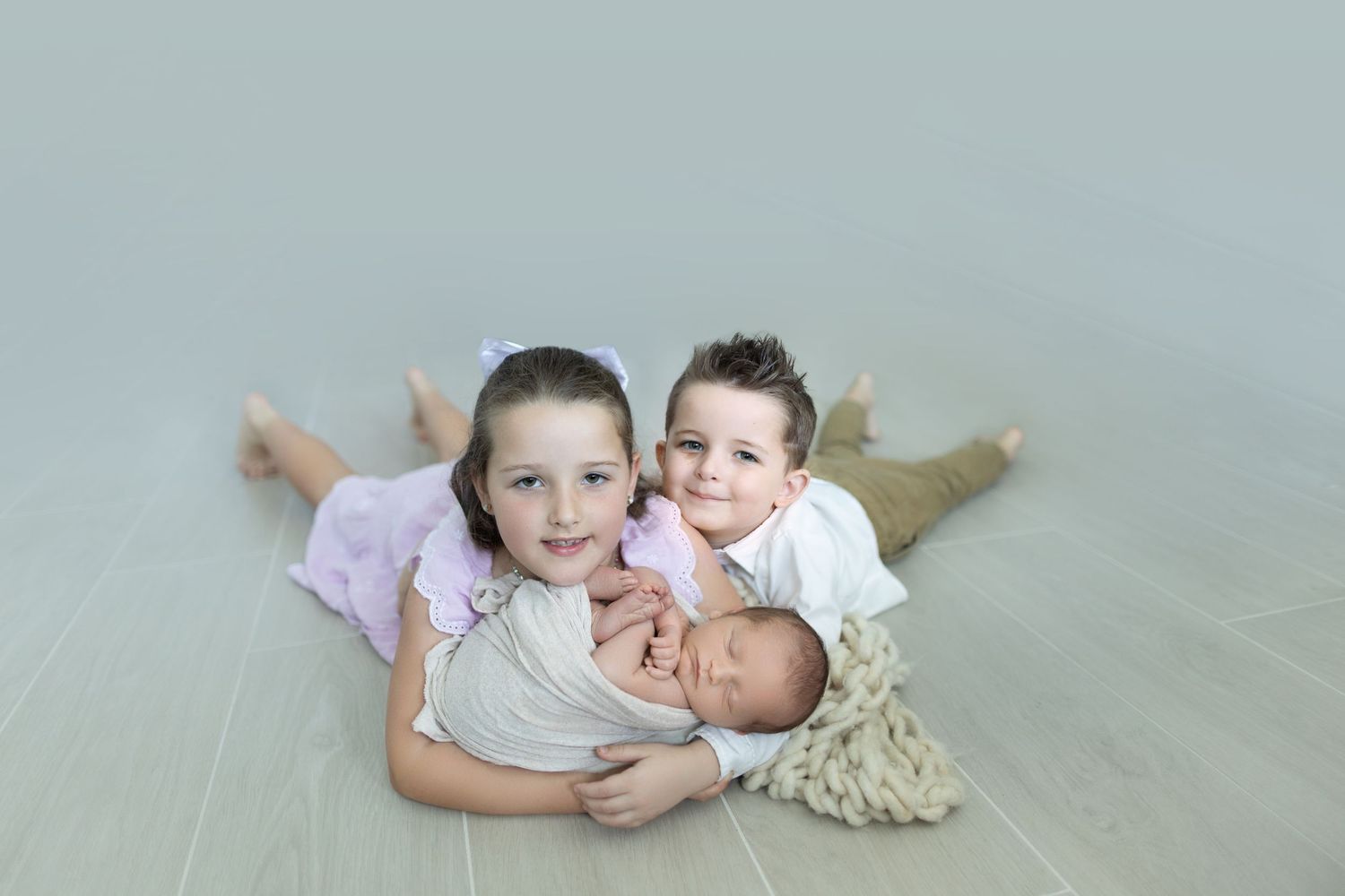 Three children lying together on light gray studio floor during portrait session. Photos by Tampa Photographer DigitalMyst Photography