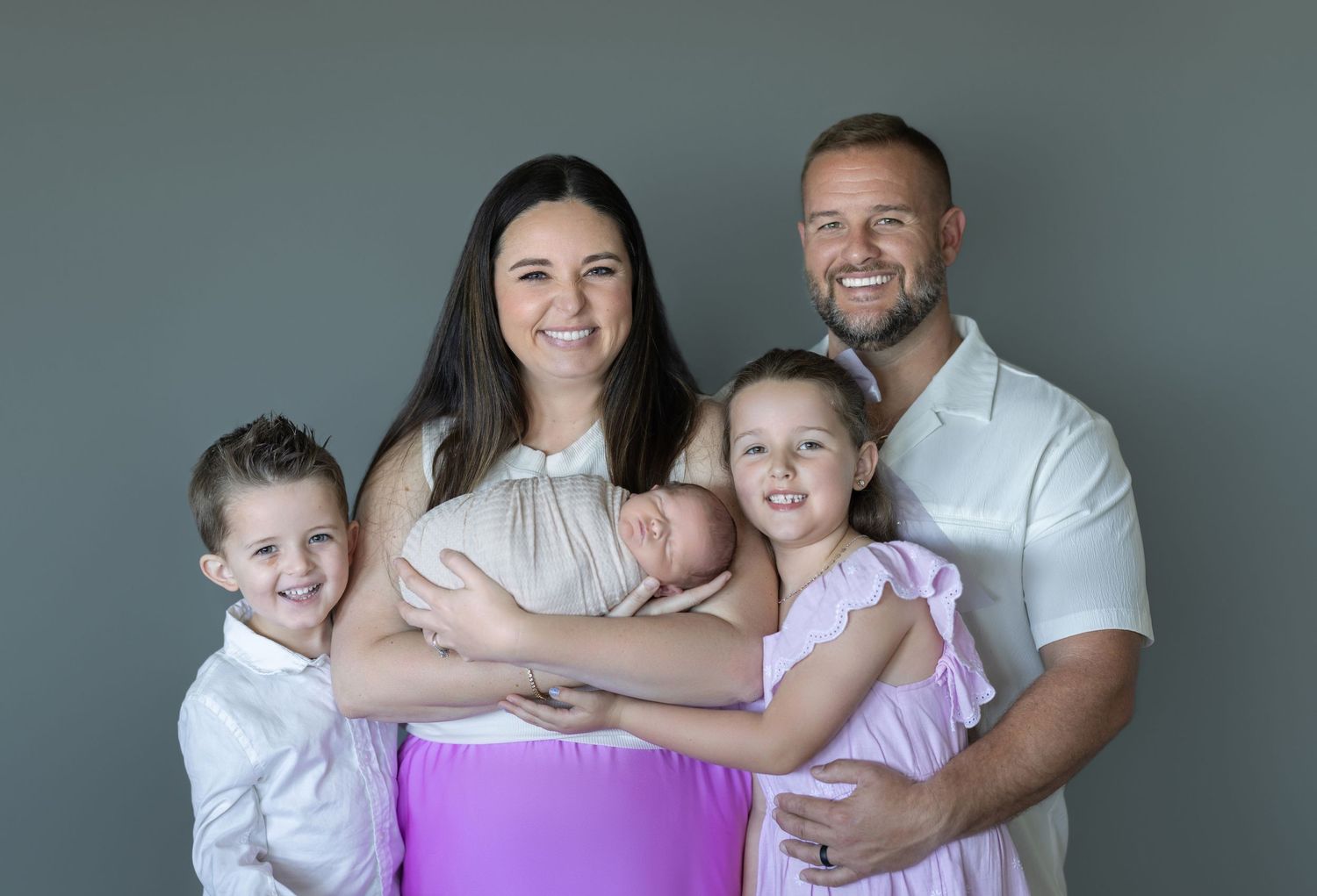 Family of five wearing coordinated outfits against gray studio backdrop.