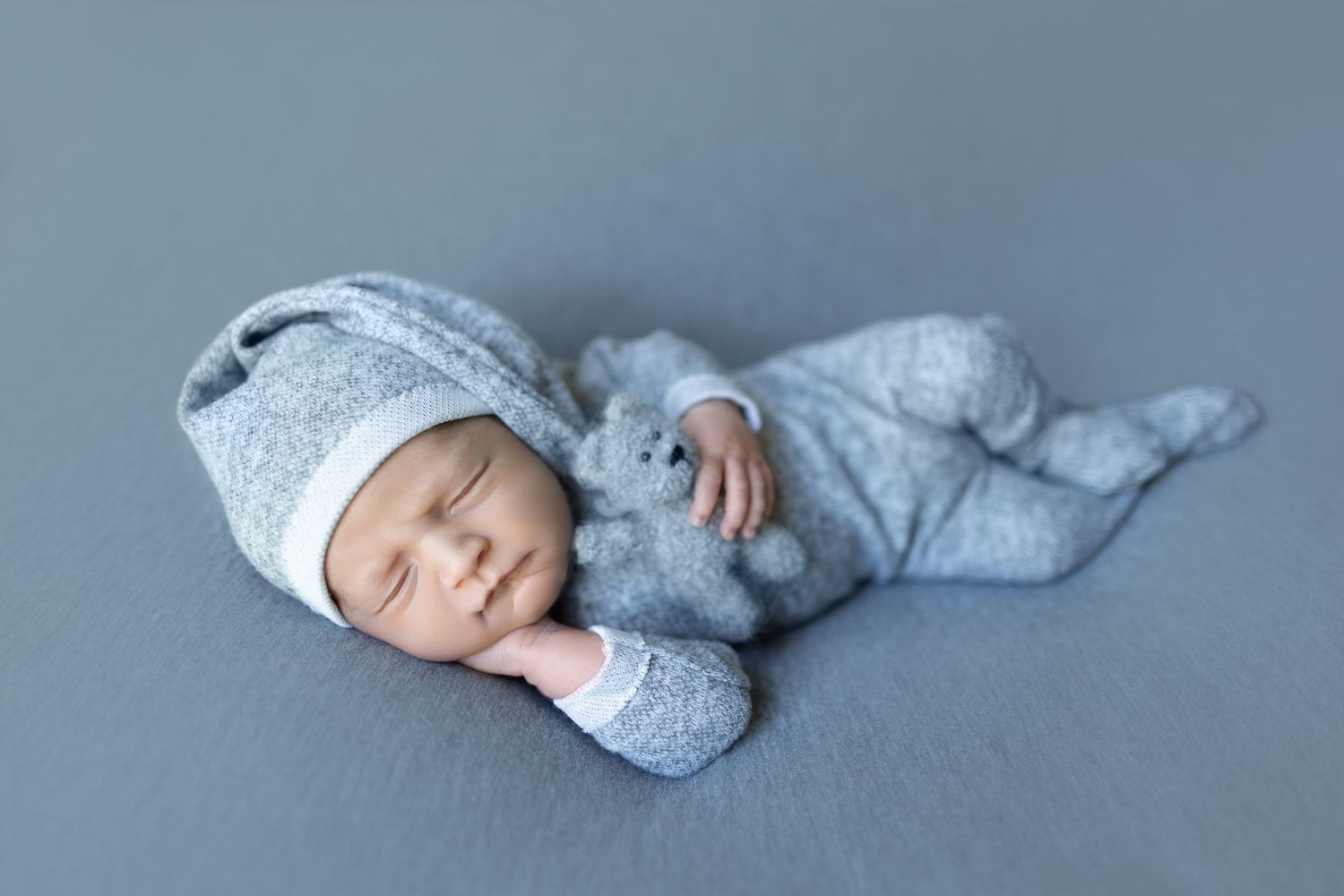 Sleeping newborn in soft gray attire lying peacefully on blue background. Photos by Tampa Photographer DigitalMyst Photography