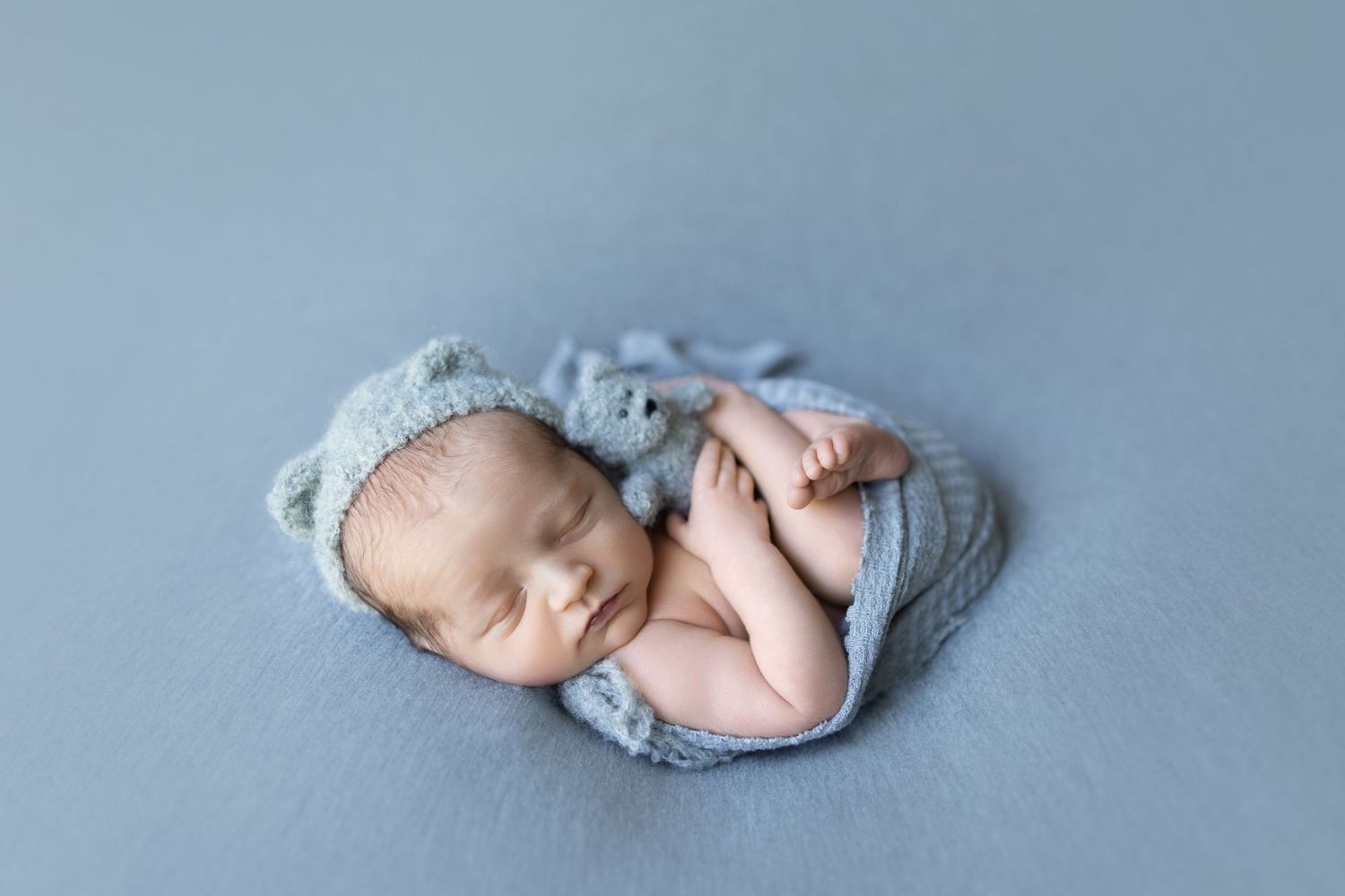 Peaceful newborn baby wrapped in blue fabric sleeping during professional photoshoot.