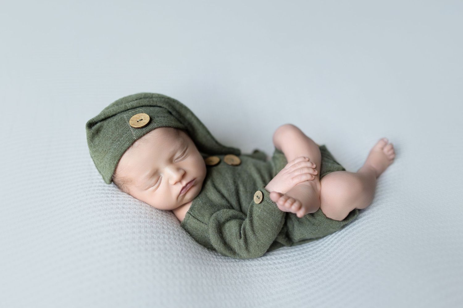 Sleeping newborn in olive green outfit and cap during professional photography session. Photos by Tampa Photographer DigitalMyst Photography