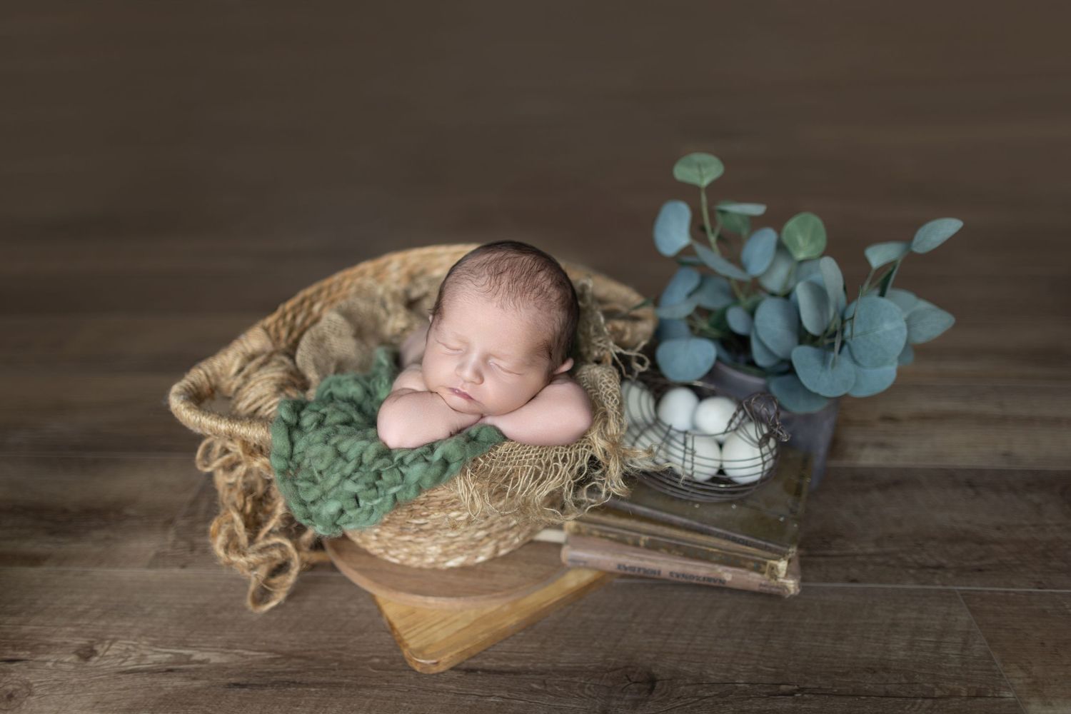 Sleeping newborn in rustic basket with decorative eucalyptus on wooden surface. Photos by Tampa Photographer DigitalMyst Photography