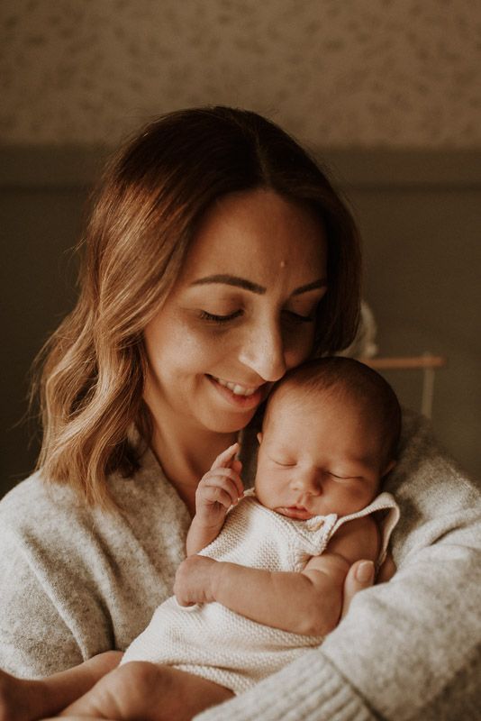 A tender moment between parent and newborn baby in warm lighting, both wearing soft white clothing.