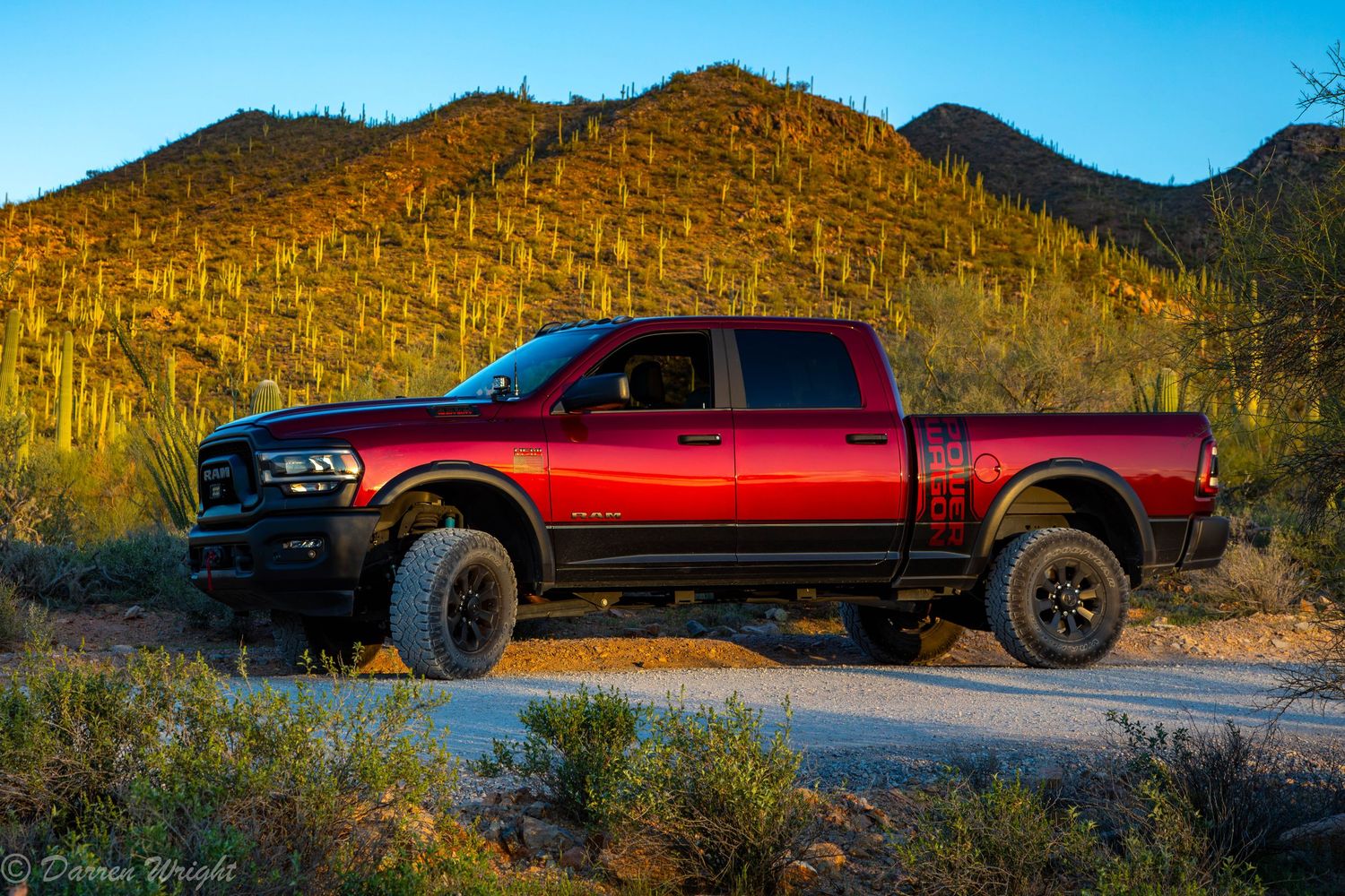 Red lifted pickup truck parked on desert road with saguaro cacti and mountains at sunset.