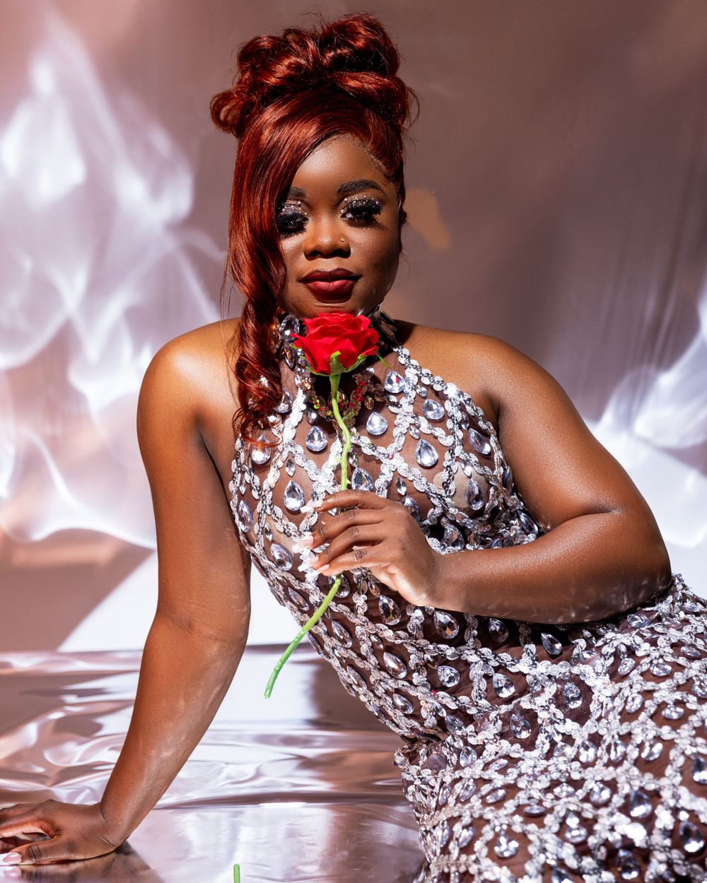 An elegant portrait with a red rose and crystalline white dress against a soft pink background.