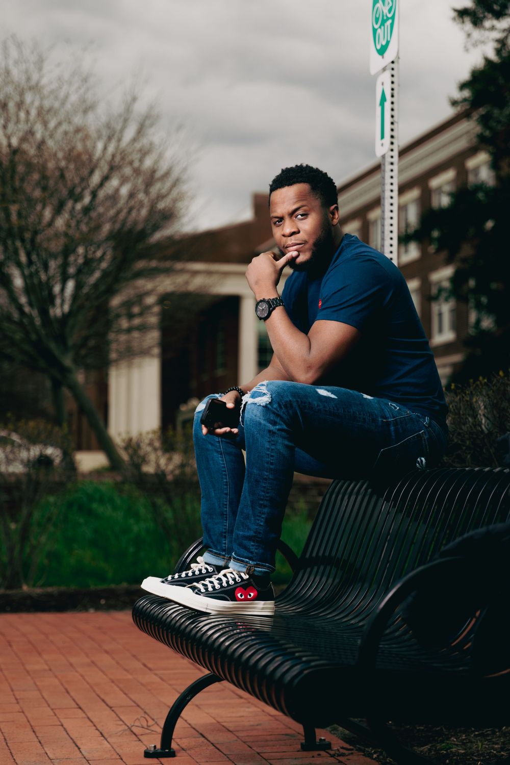 Someone in a navy blue shirt and jeans sits contemplatively on a black metal bench in an urban setting.