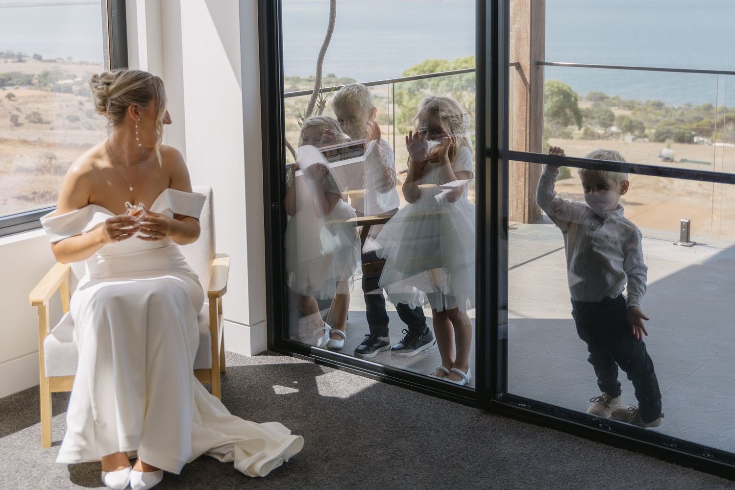 Wedding party members gather outside a venue with large windows overlooking a scenic landscape.