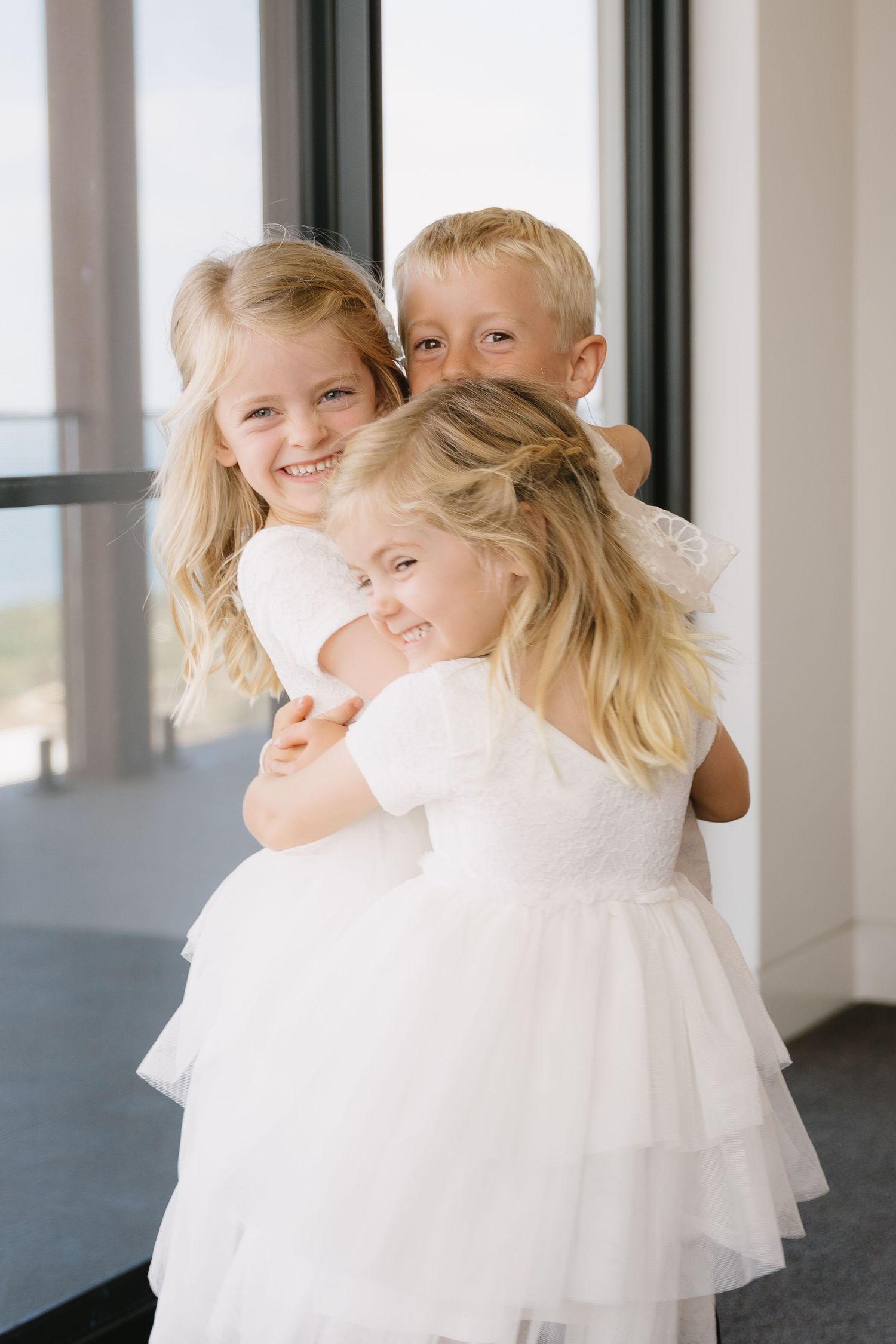 Children in white formal attire playing and twirling on a dark floor during wedding celebrations.