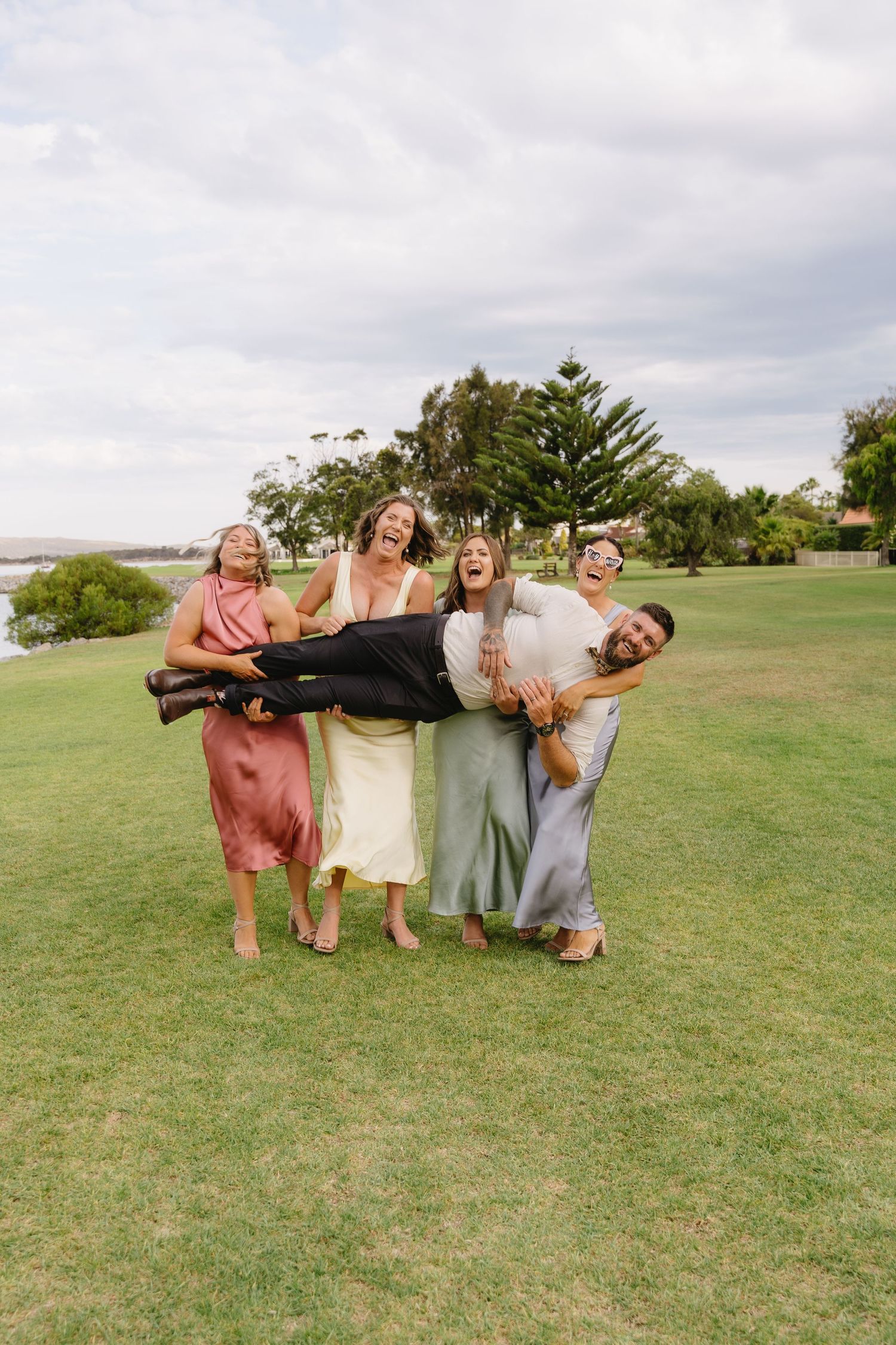 Wedding party members strike fun poses on a green lawn.