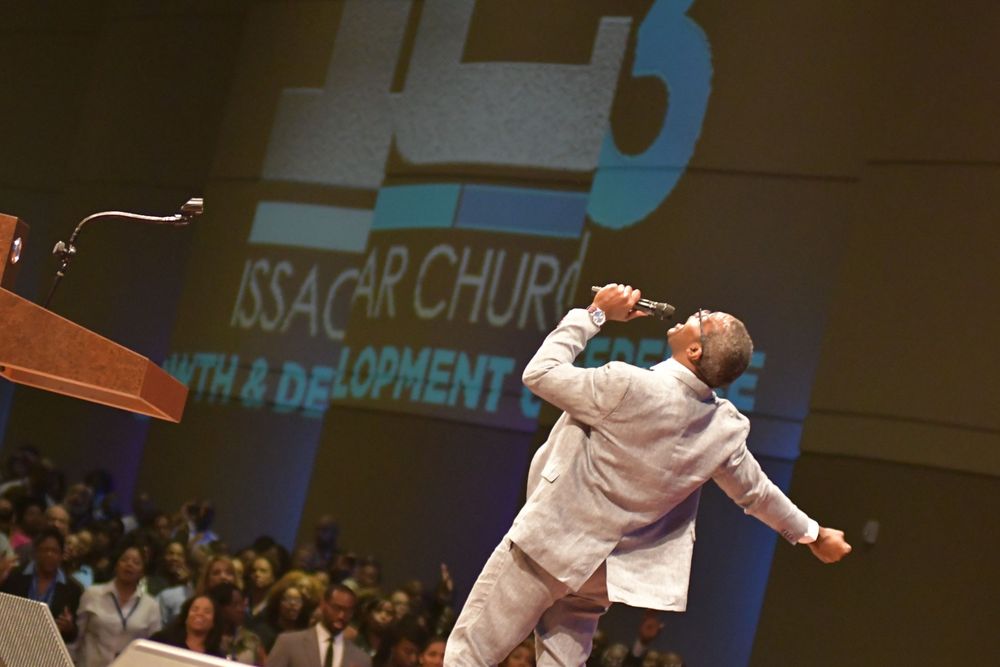 Performer in white outfit singing passionately on stage at a church event with illuminated text projection behind them.