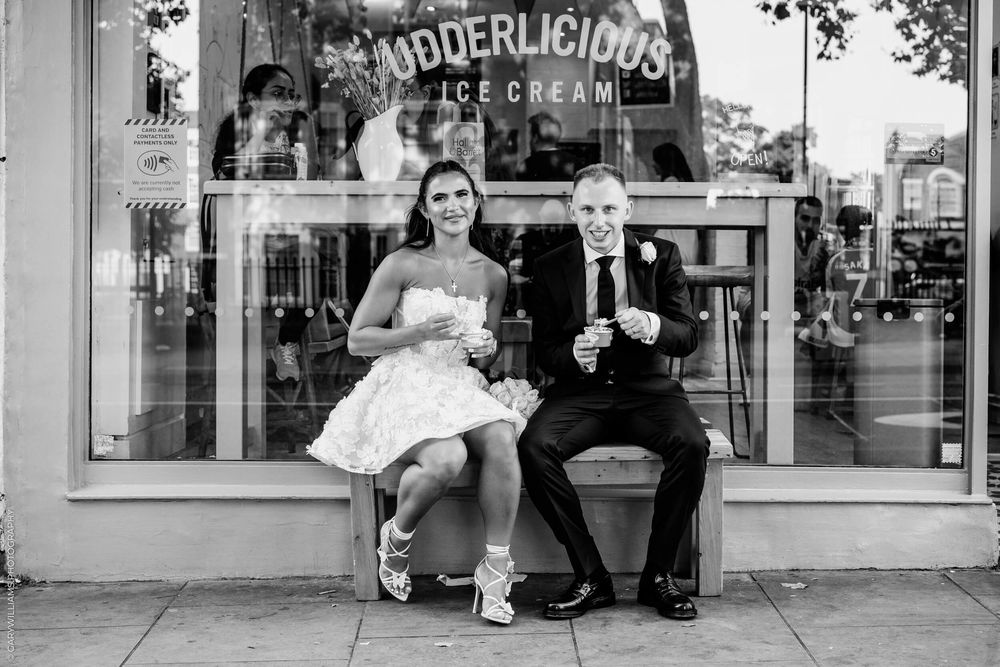Two people sit on a bench outside a storefront window sharing ice cream cones in black and white photography.