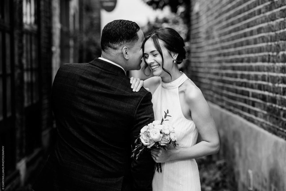 Black and white romantic wedding photo of a couple sharing an intimate moment against a brick wall.