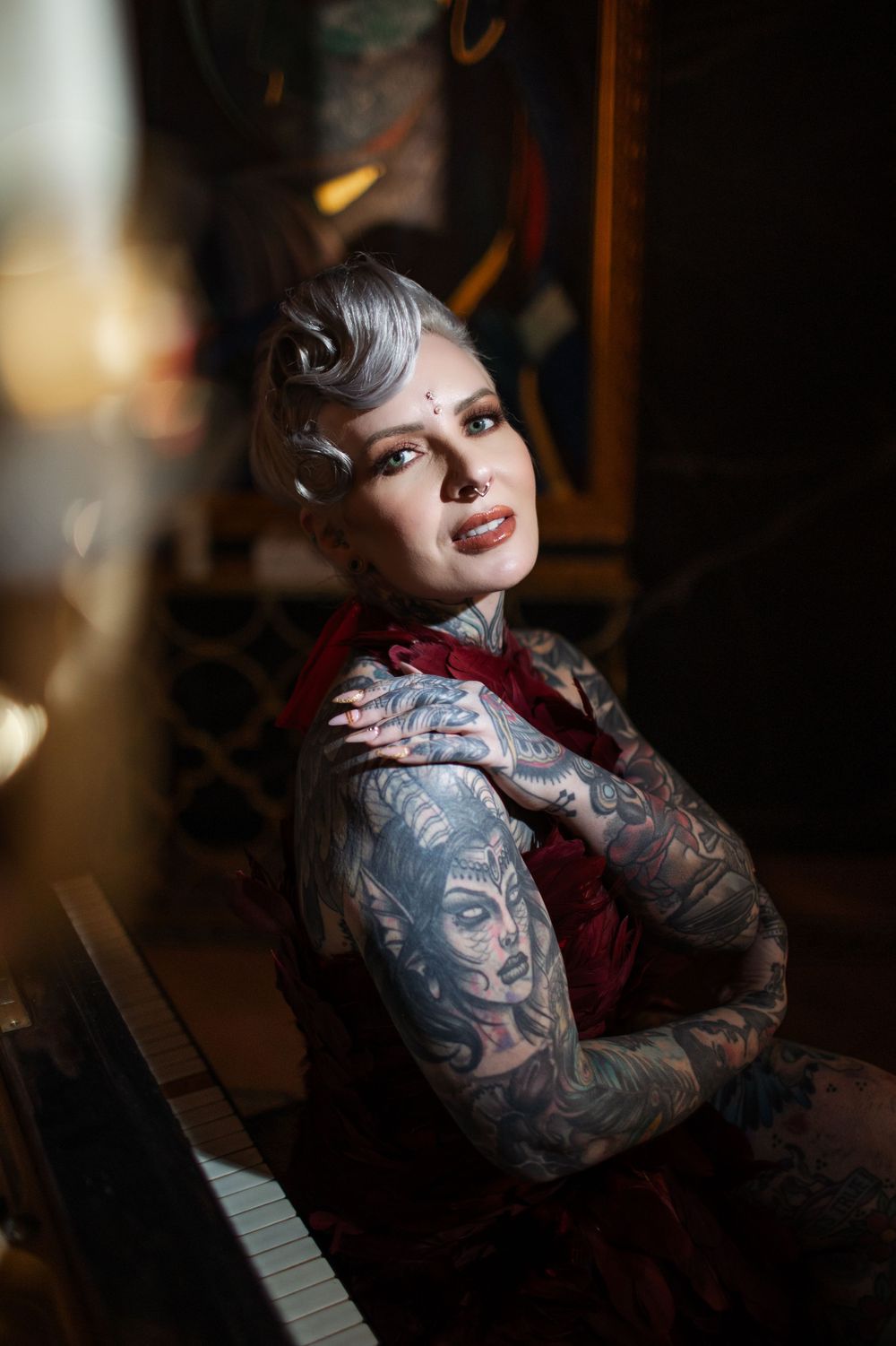 An artistic portrait featuring tattoo art and a deep red vintage dress in moody lighting.