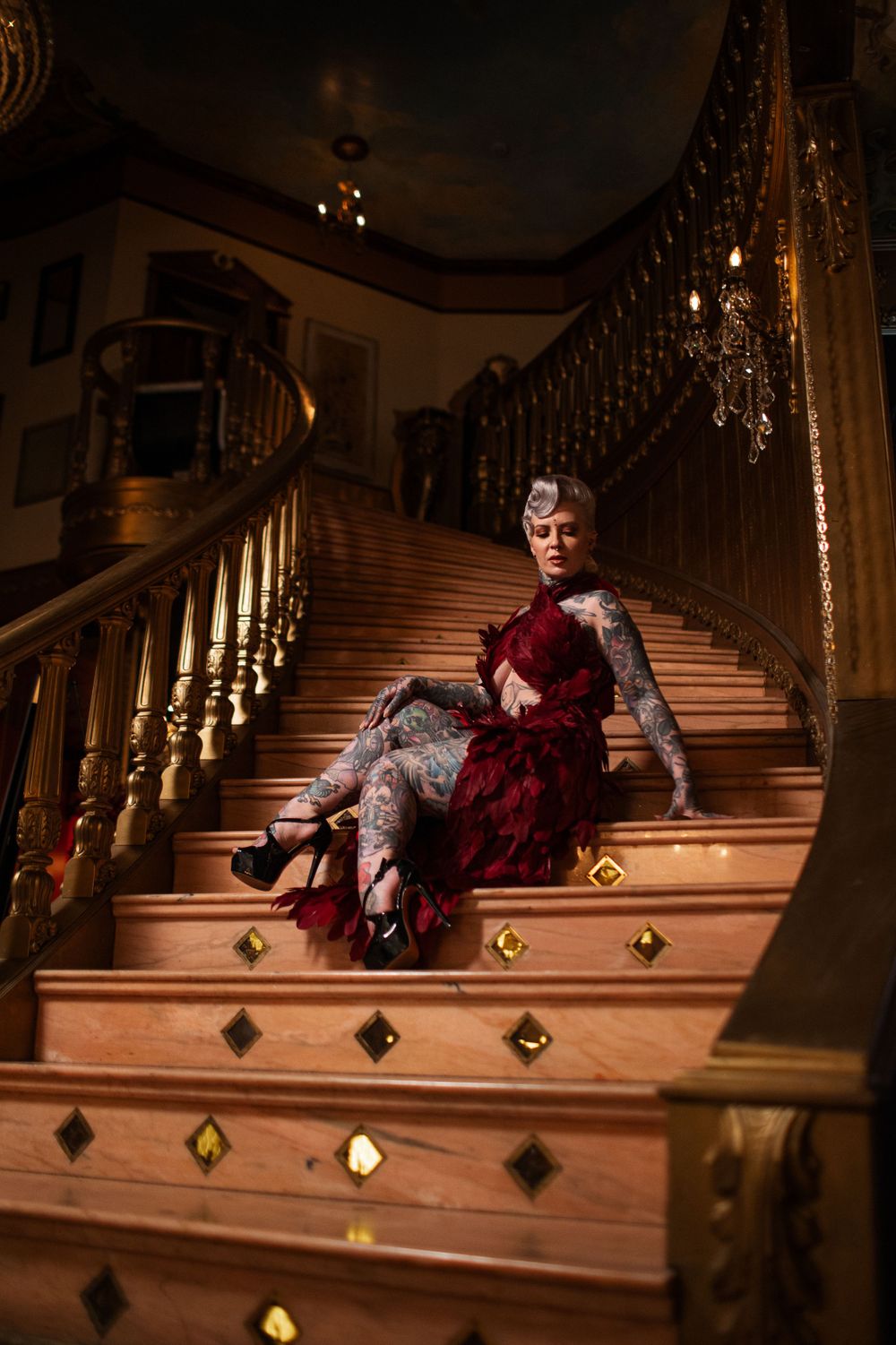 A dramatic pose on illuminated stairs featuring a flowing red dress and vintage interior design elements.