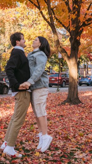 Couple sharing an intimate moment under vibrant fall foliage with cars parked along the street.