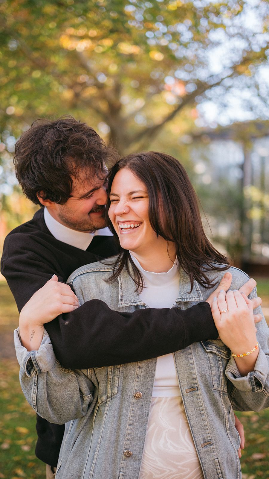 Couple sharing a joyful embrace outdoors during autumn with fall foliage in the background.
