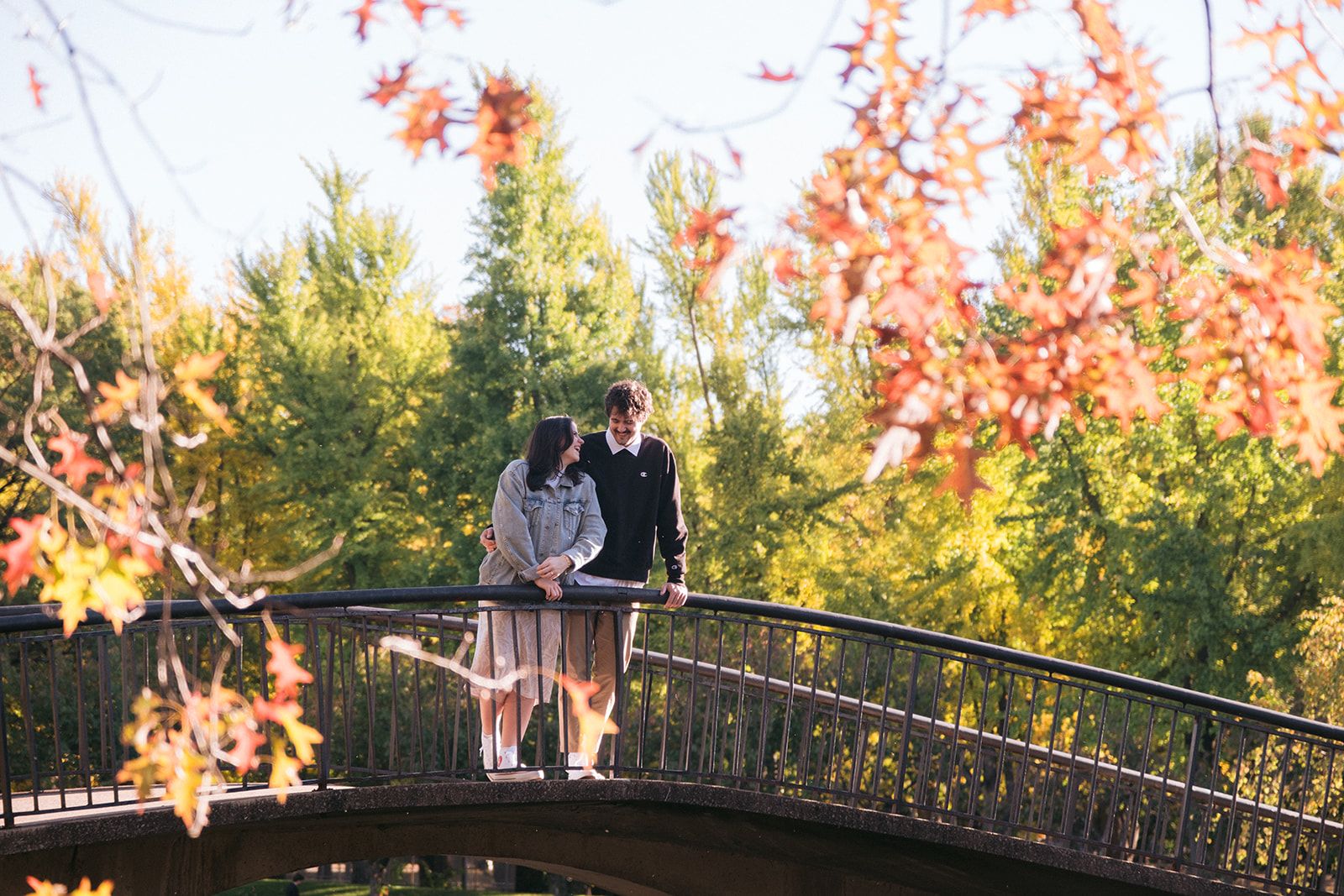 A couple shares an intimate moment on an arched bridge surrounded by vibrant autumn foliage at sunset.