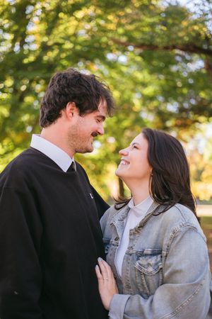 A romantic couple shares a tender moment outdoors with autumn foliage in the background during golden hour.