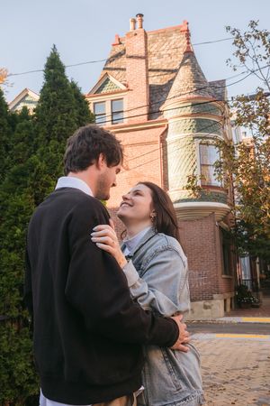 A romantic scene shared between a couple in front of a beautiful brick Victorian house.