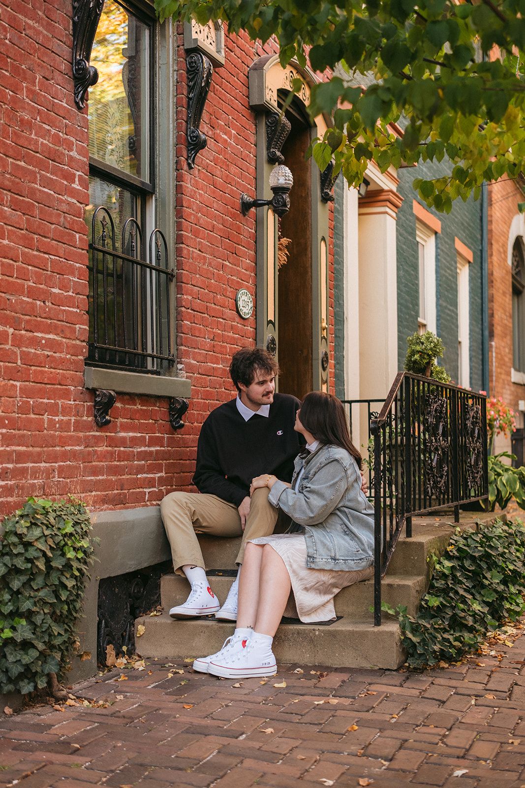 A couple sits together on brick steps in front of historic brownstone homes during autumn in Georgetown.