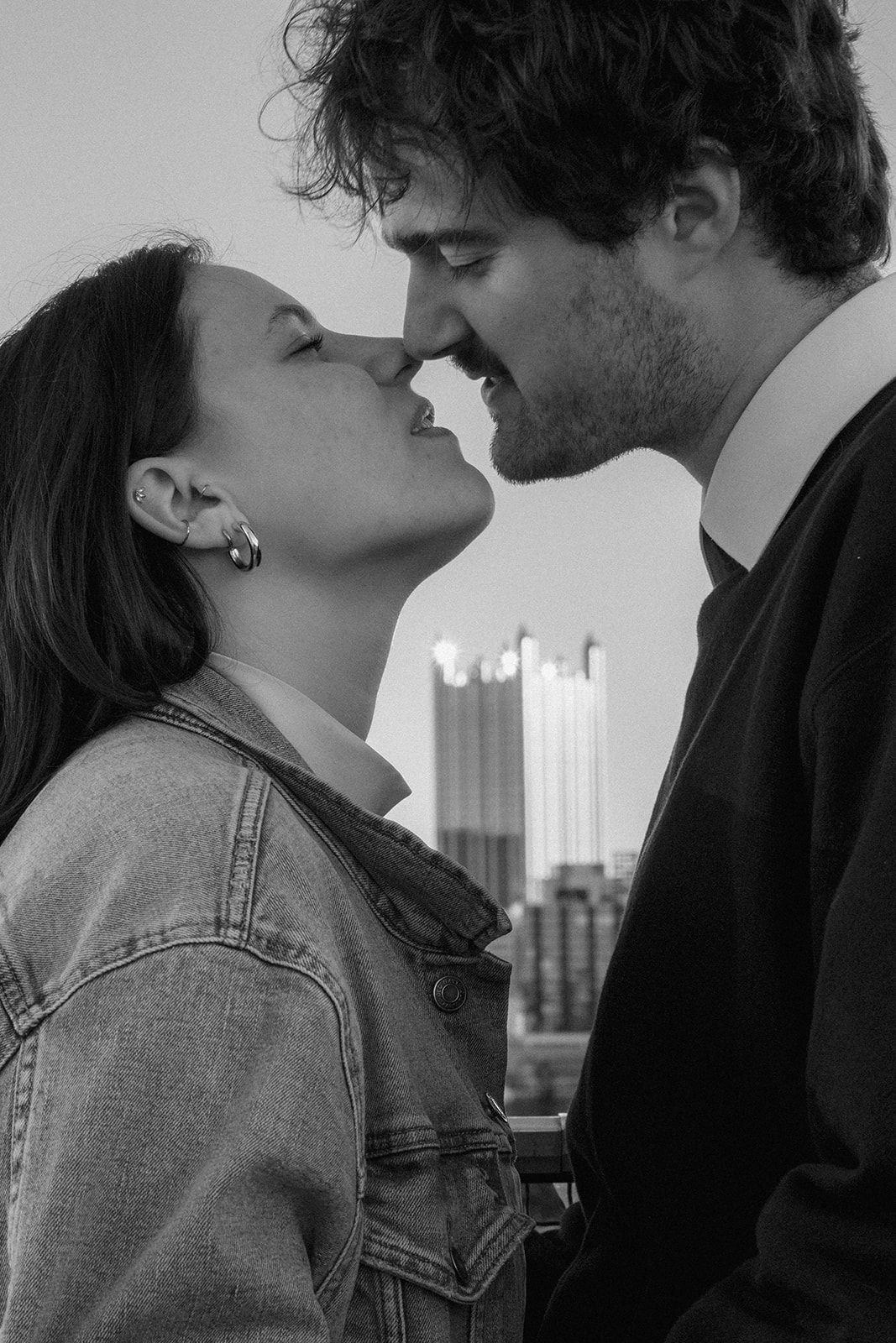 A black and white portrait of a couple in an intimate moment with Pittsburgh's downtown architecture behind them.