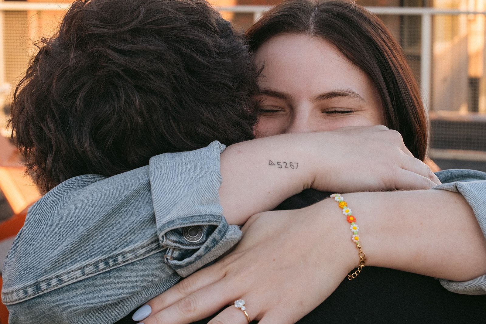 Close-up of an embrace showing clasped hands wearing a bracelet and denim jacket sleeve.
