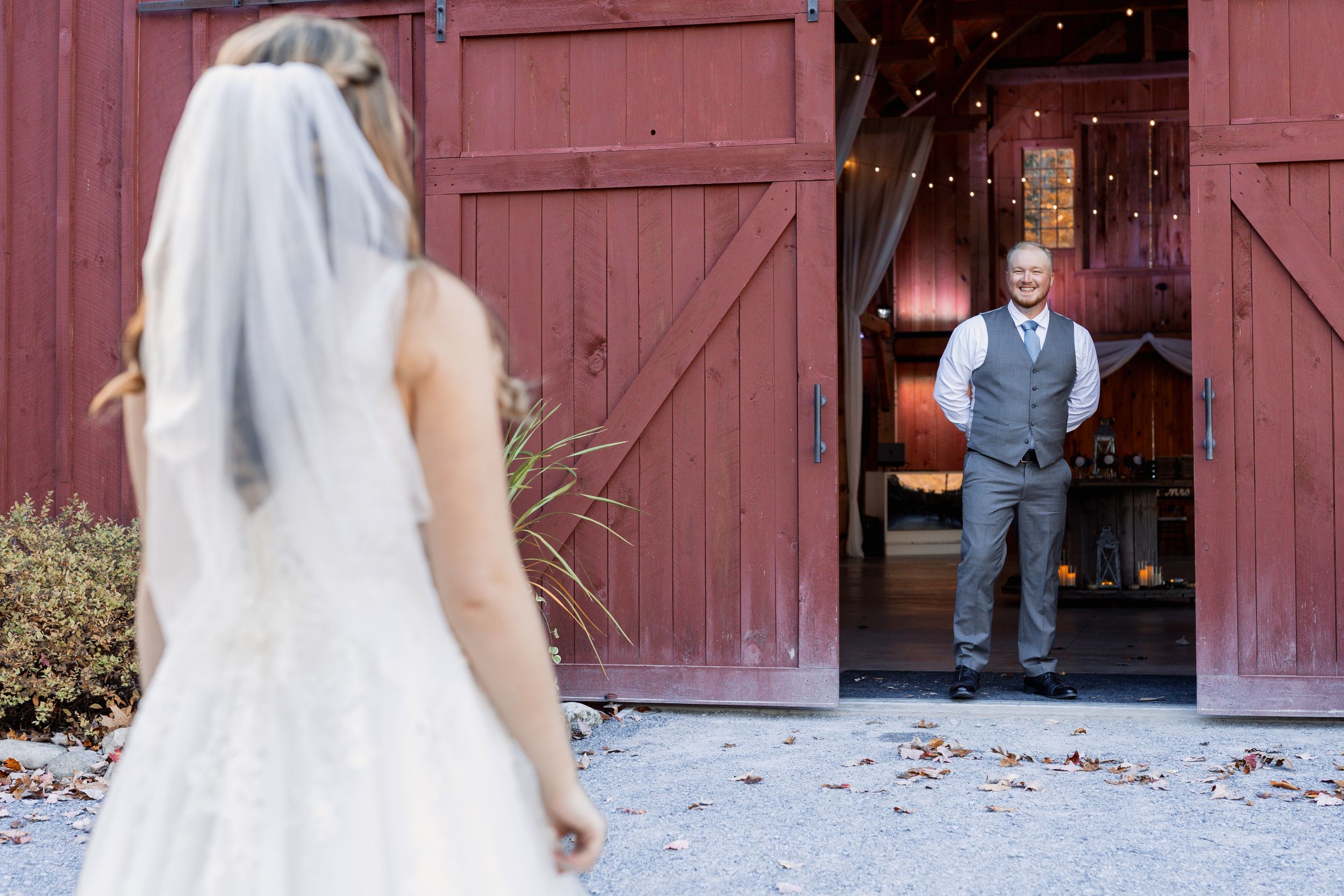 First look moment captured outside red barn doors with twinkling lights.