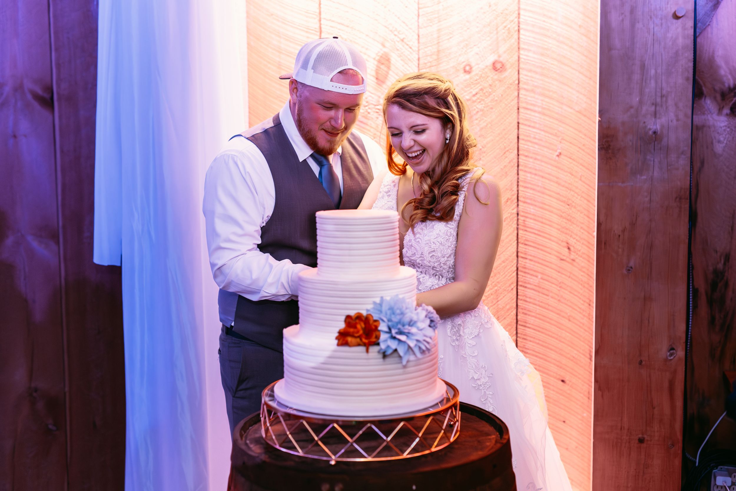 Couple cuts elegant white wedding cake together at rustic barn reception.