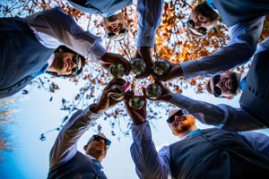 Groomsmen toast with drinks in creative low-angle circle shot against autumn sky.
