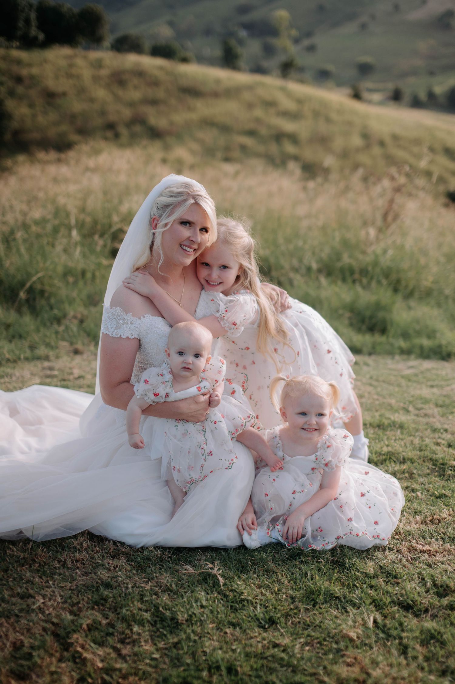 Wedding portrait on grassy hillside with bride and children in matching dresses.