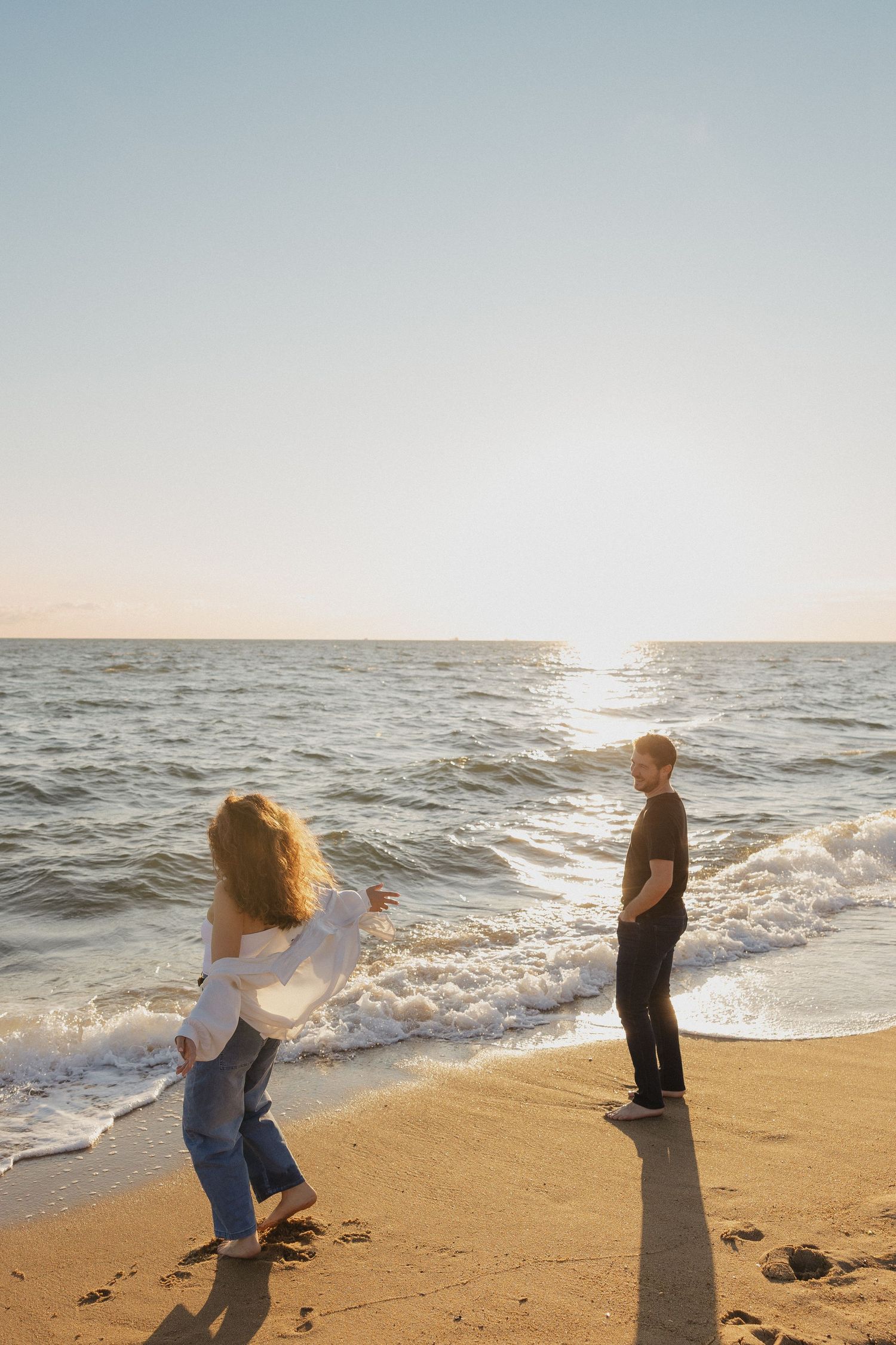 A couple embraces in a golden field during sunset while wearing cozy sweaters.