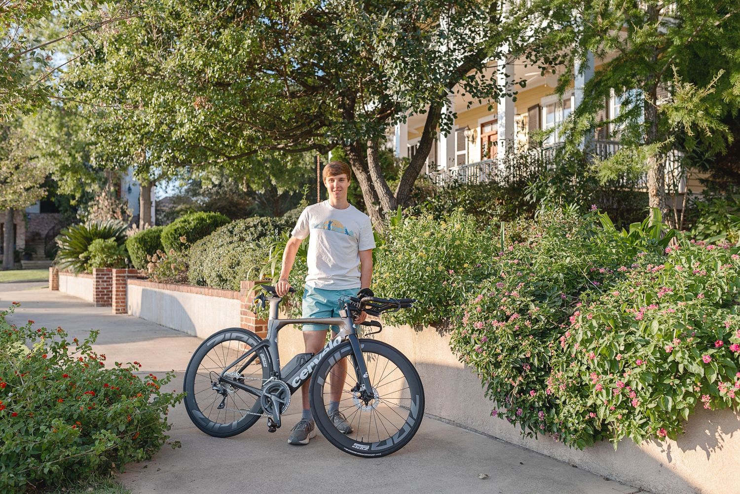 Cyclist with blue bike standing on tree-lined residential street.