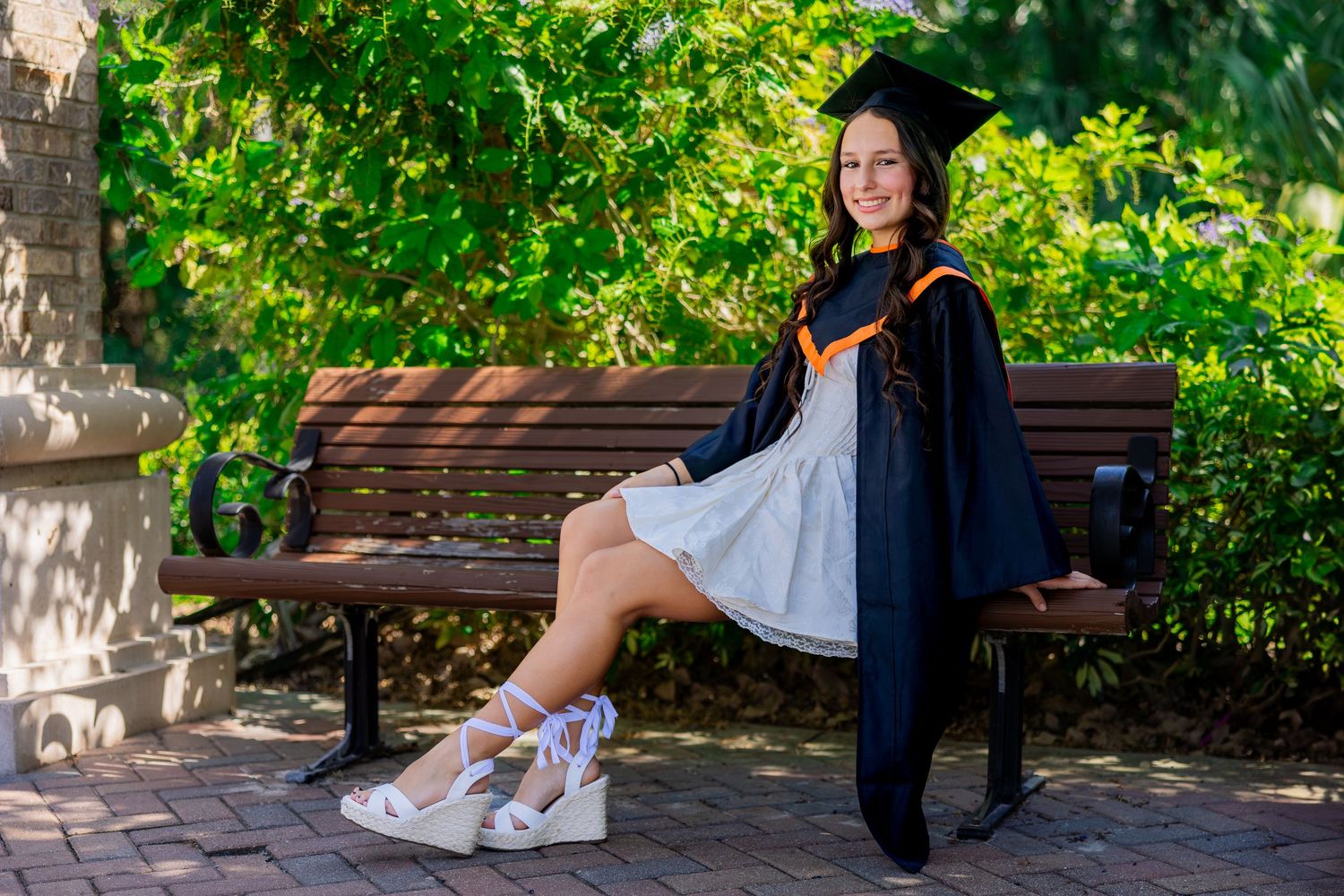 Graduate wearing green cap and gown with light blue dress and brown cowboy boots poses by a lake. Oviedo, Florida
