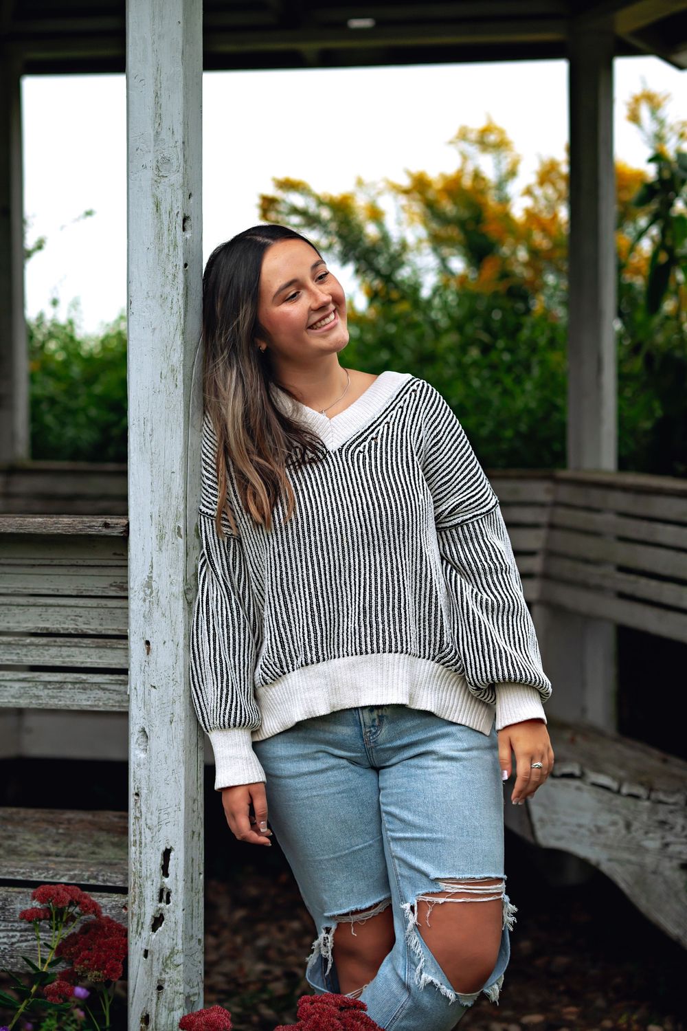 A casual outdoor portrait showing a striped sweater and ripped jeans against a rustic wooden background.