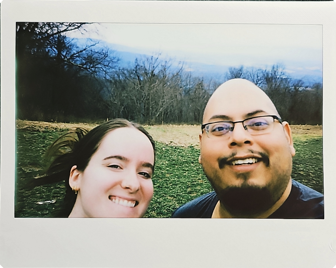 Casual outdoor selfie photo taken in a grassy field with trees in background.