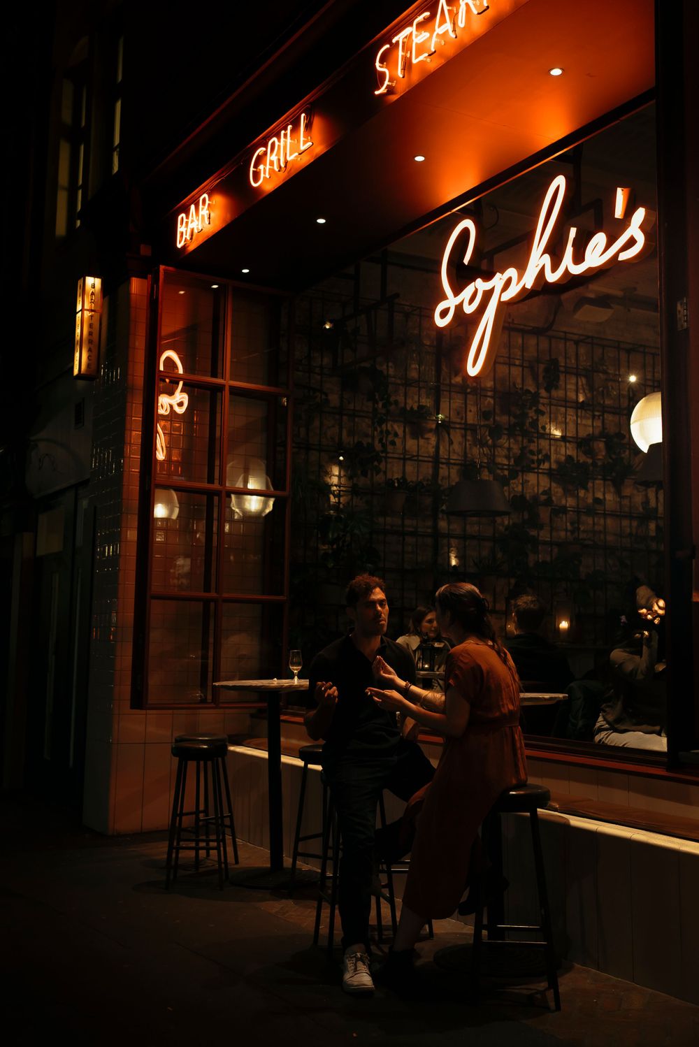 Two people chatting over a drink outside Sophie's Steakhouse, Soho London. Captured by Shayla Bloom Photography