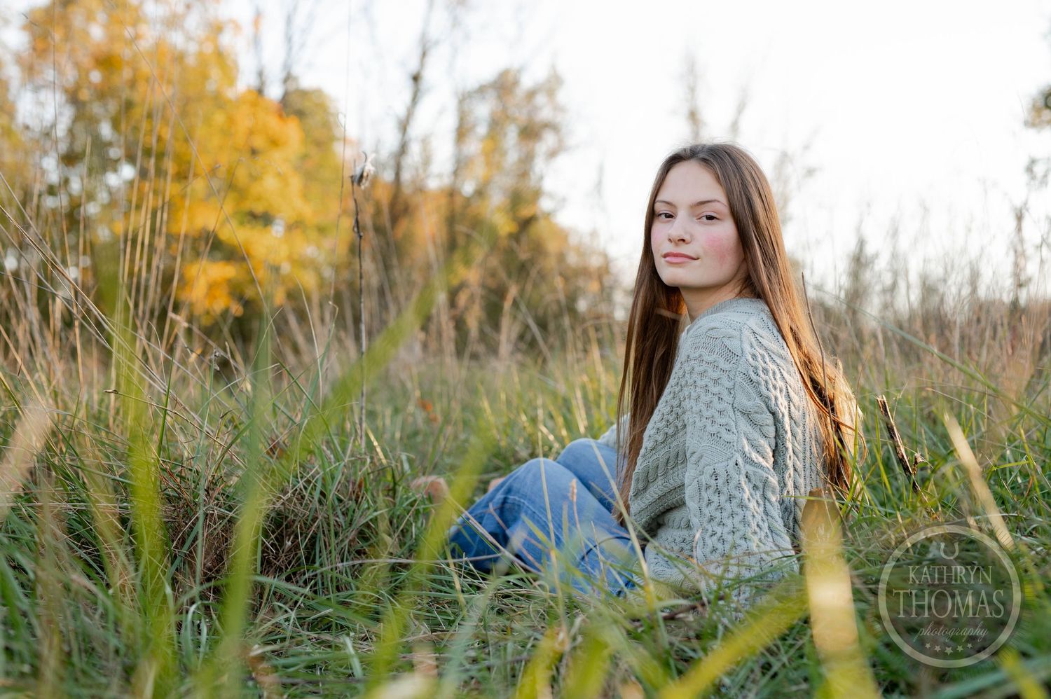 Outdoor portrait in tall grass with autumn colors and golden light in the background.