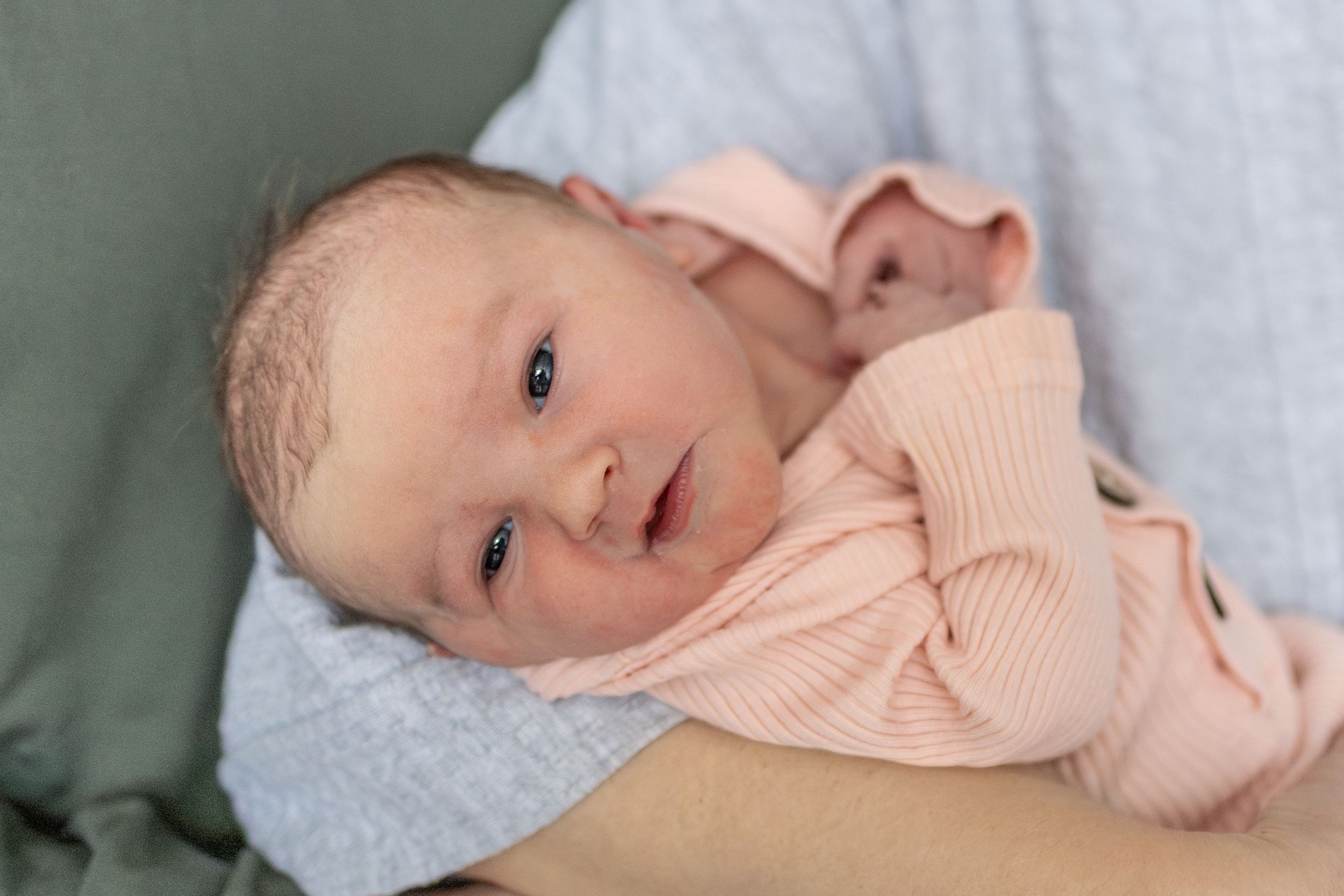 Newborn baby looking at the photographer while being held in moms arms