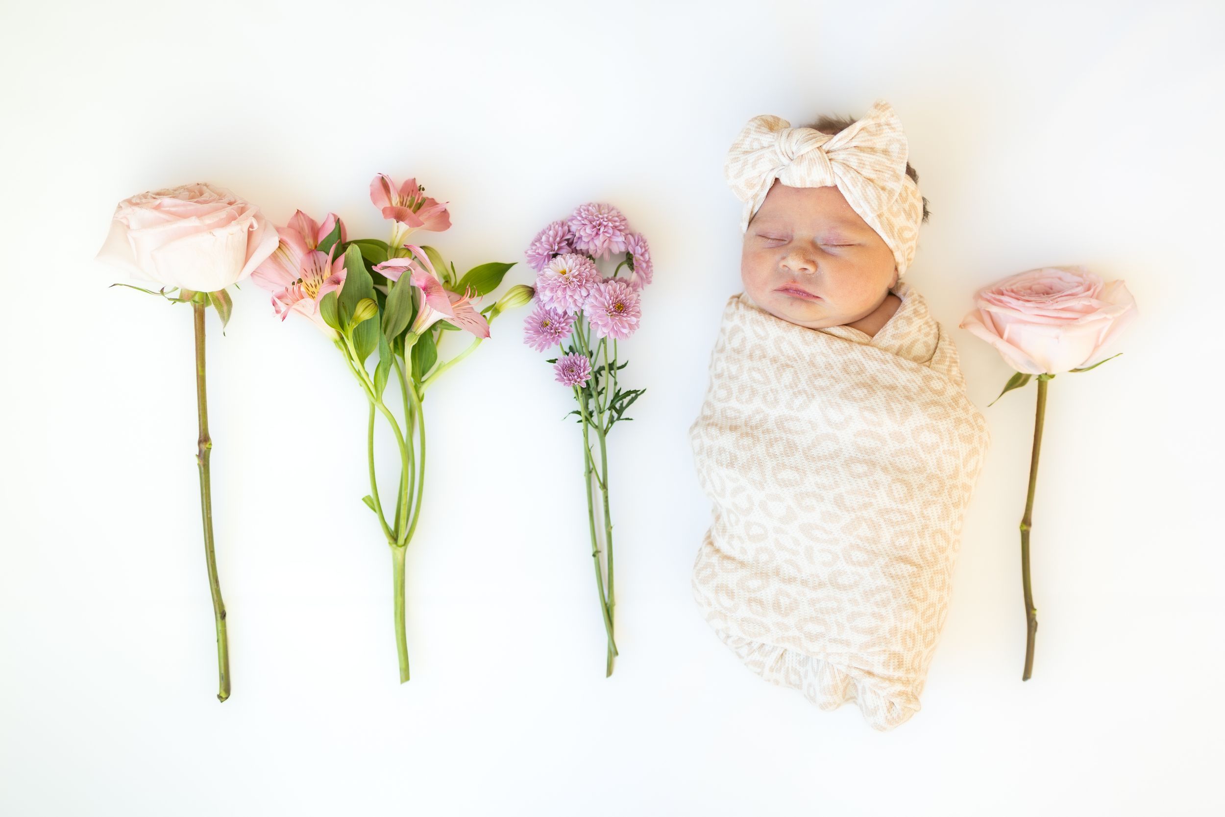 Newborn baby laying on a white blanket with flowers alongside her