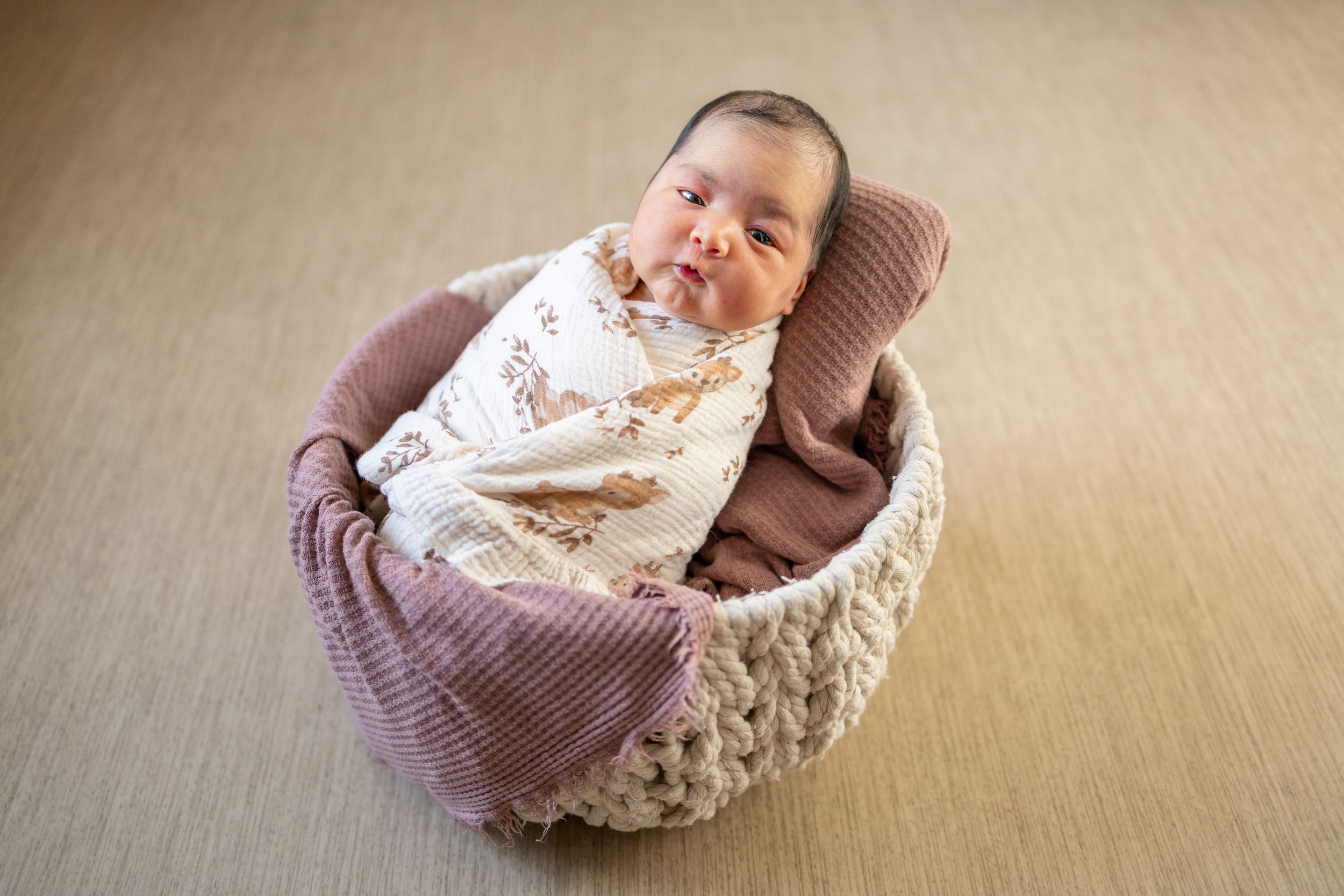 Newborn baby looking at the photographer while propped on a mauve blanket in a white rope basket