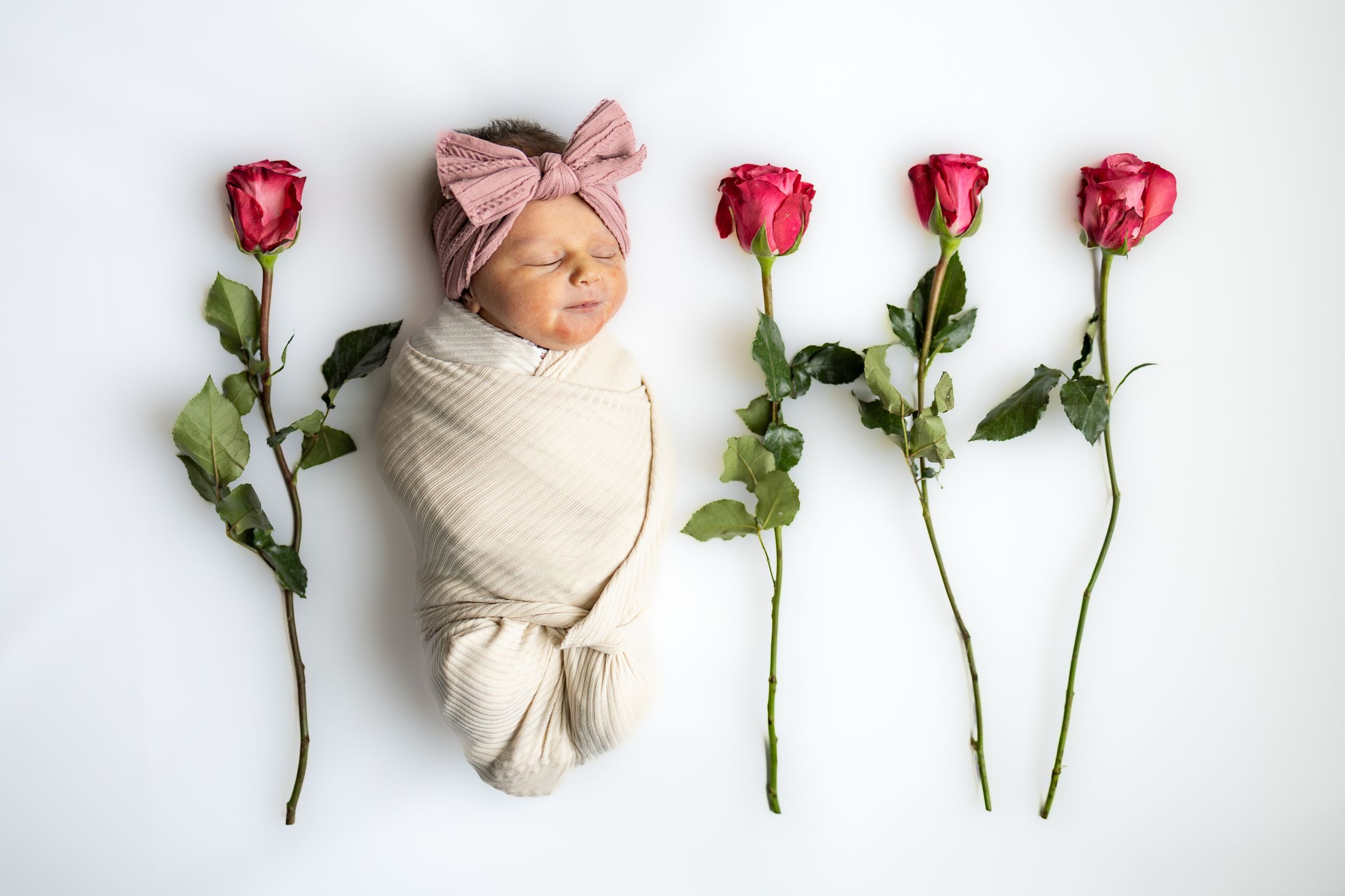 A series of newborn photography images showing a baby swaddled in white fabric alongside pink roses and green stems.