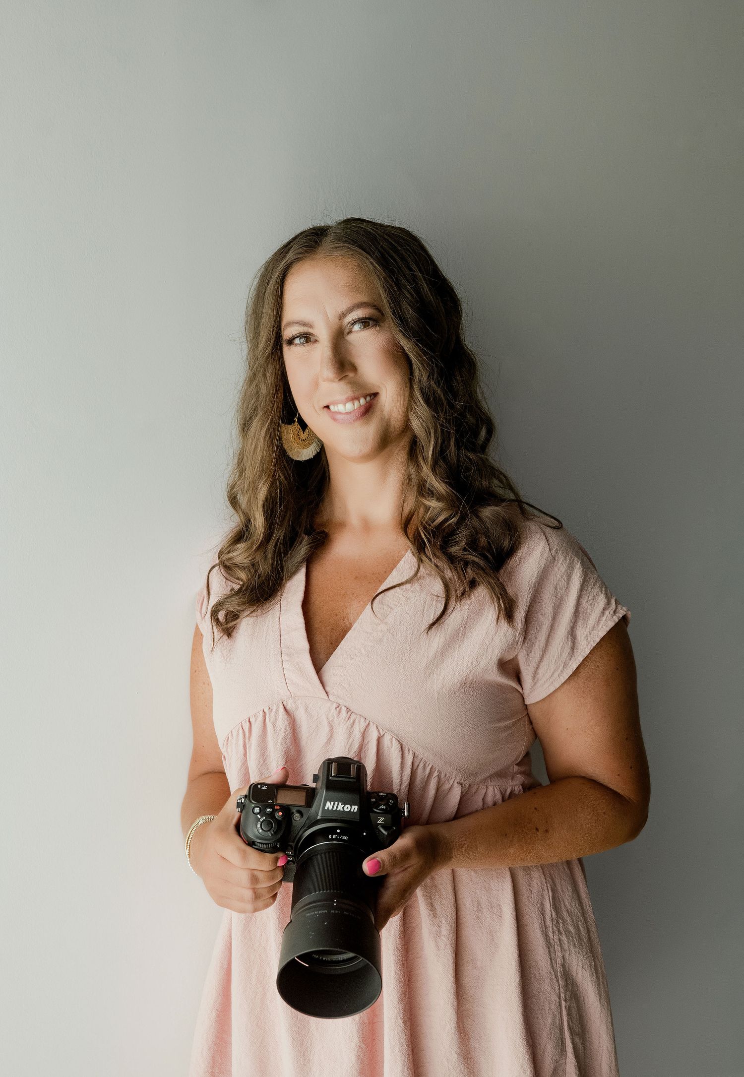 Person in pink dress holding professional camera against grey background.