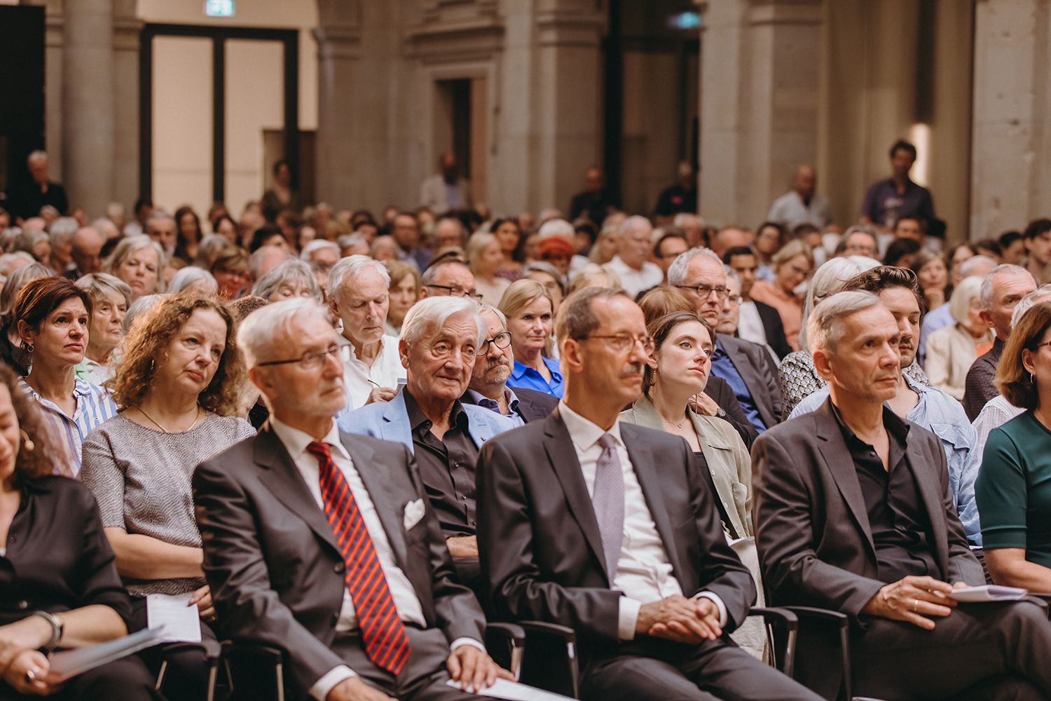 Large audience seated in an ornate hall during a formal event.