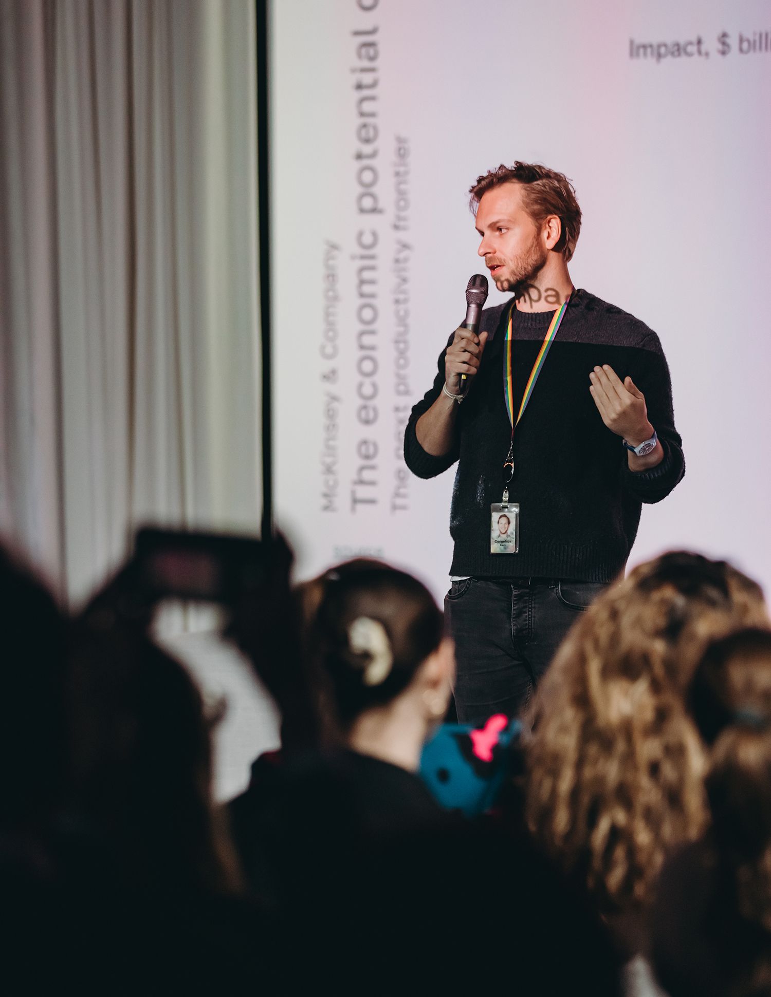 A speaker presenting on stage to a darkened audience at a conference event.