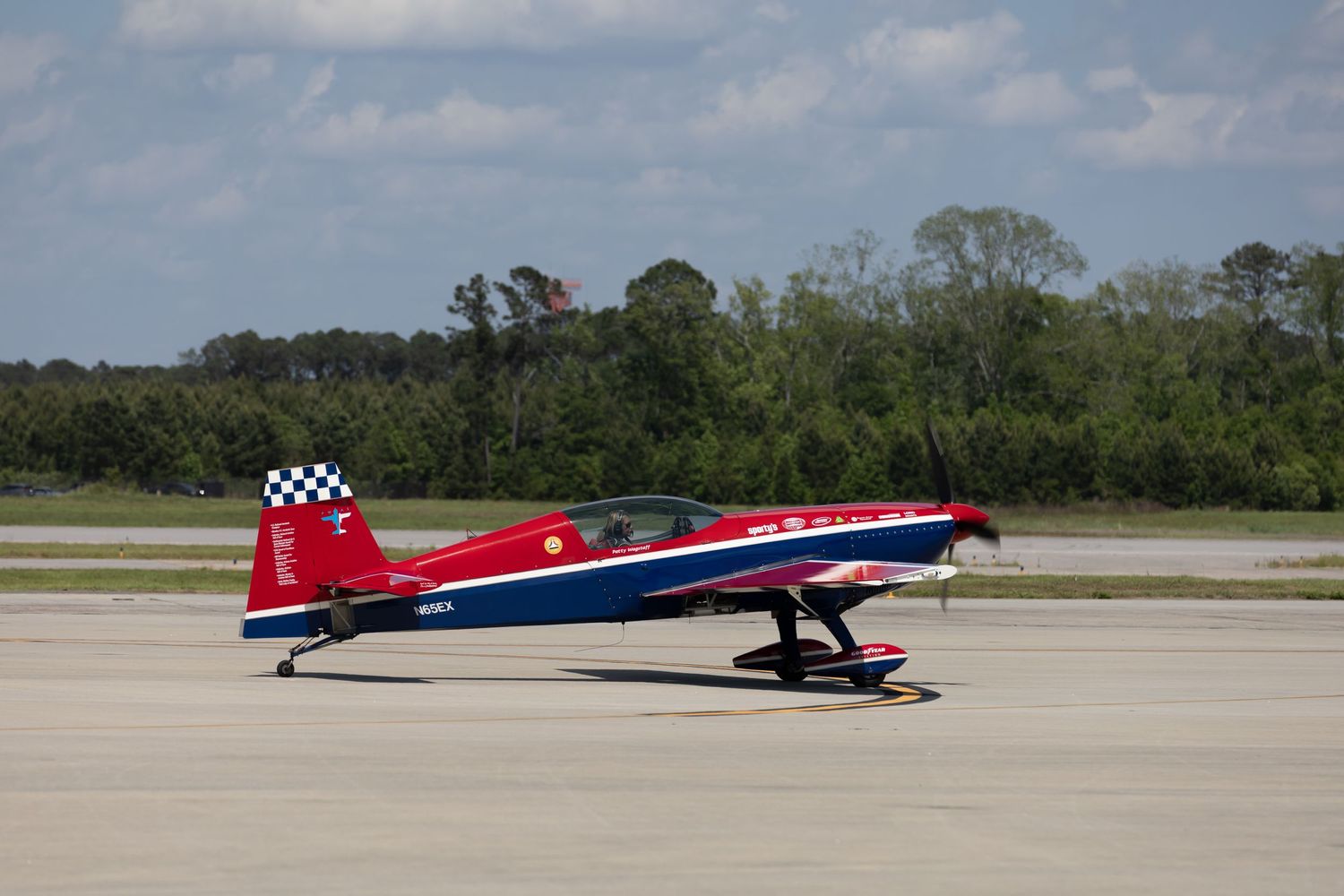 Red and blue aerobatic plane parked on tarmac under clear blue sky.