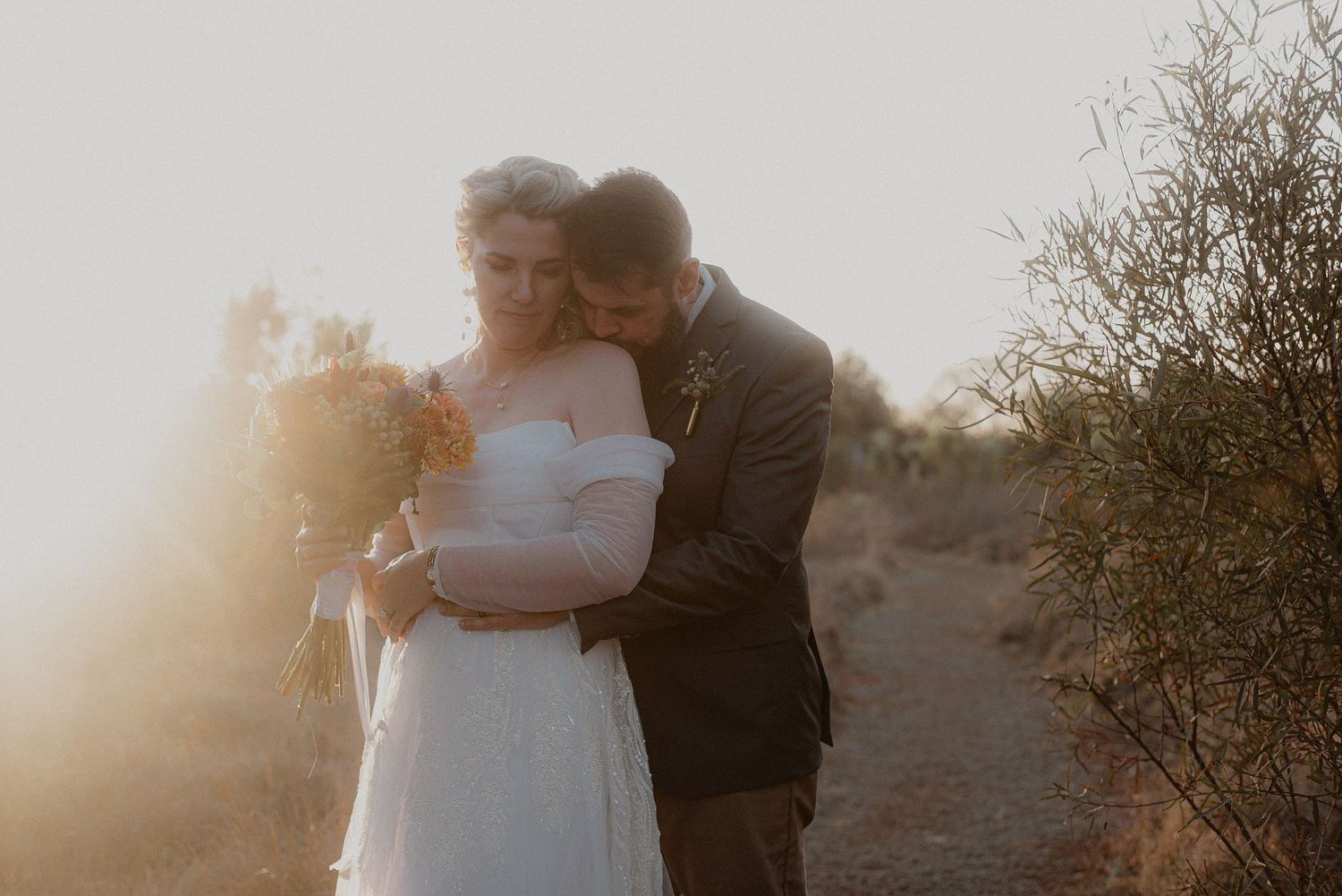 A romantic embrace between newlyweds in a desert landscape at golden hour.