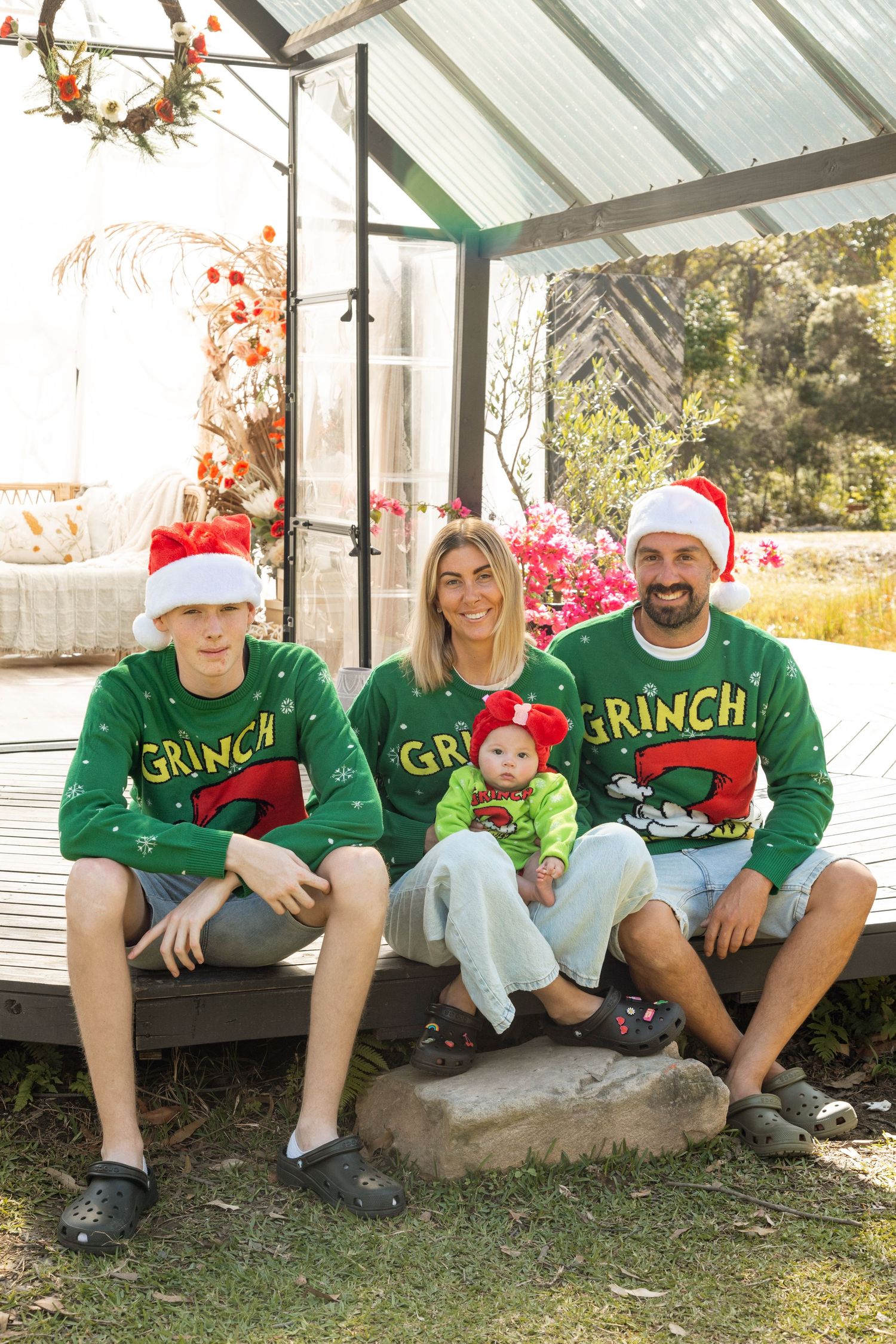 Family wearing matching Grinch Christmas sweaters sitting together outdoors.