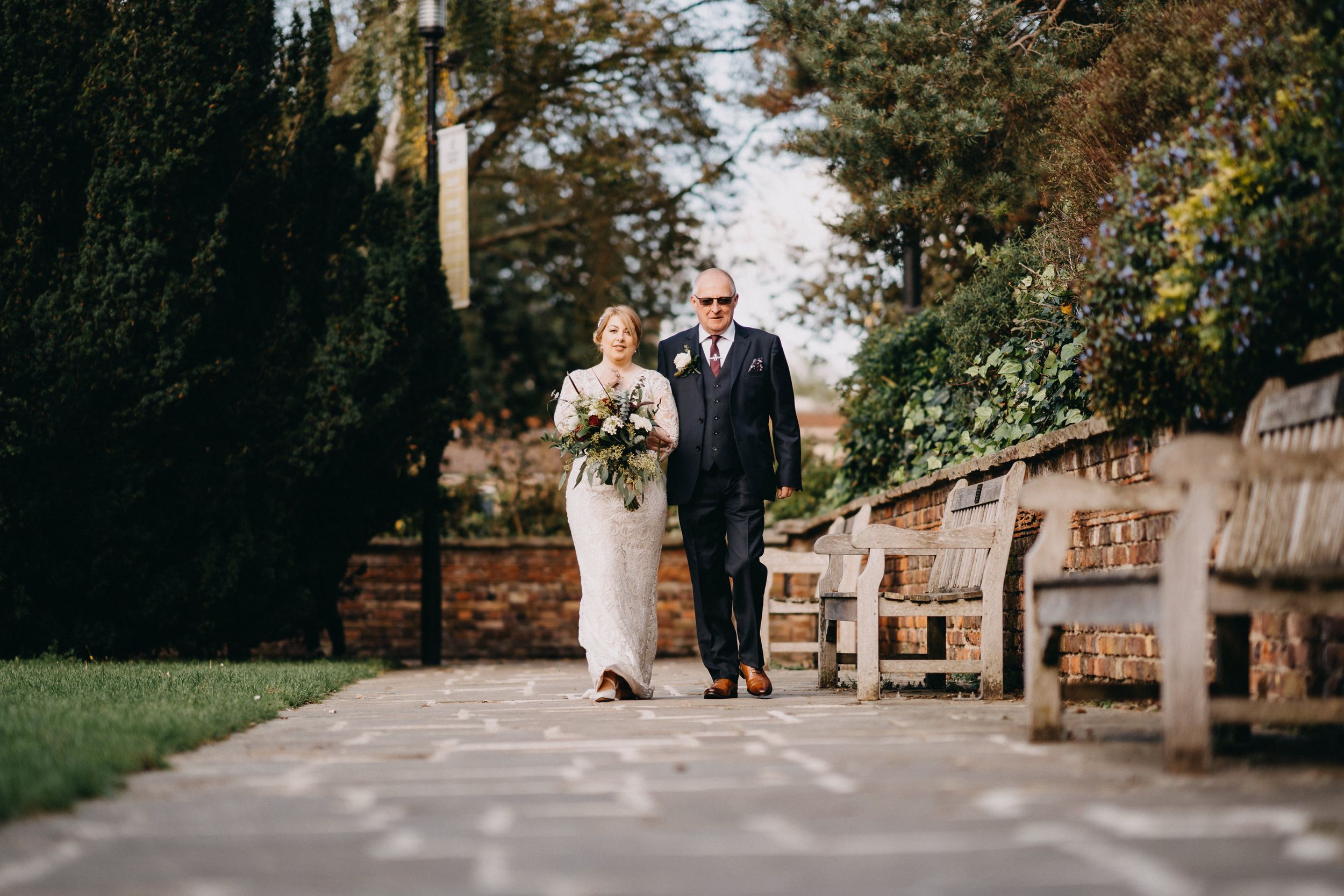 Elegant couple walking along garden path with stone benches.
