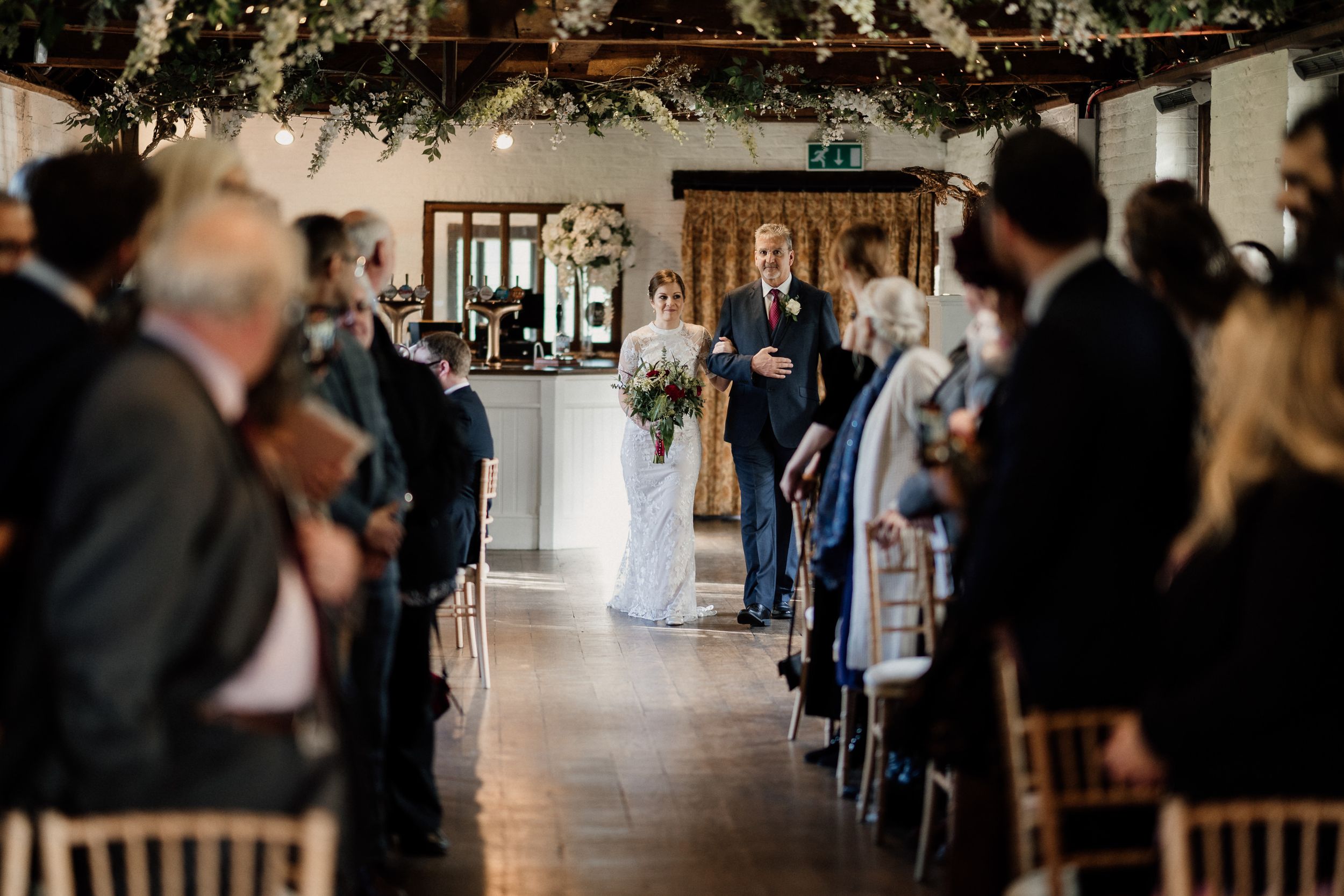 Wedding ceremony in progress inside bright venue with floral decorations at Tudor Barn London.