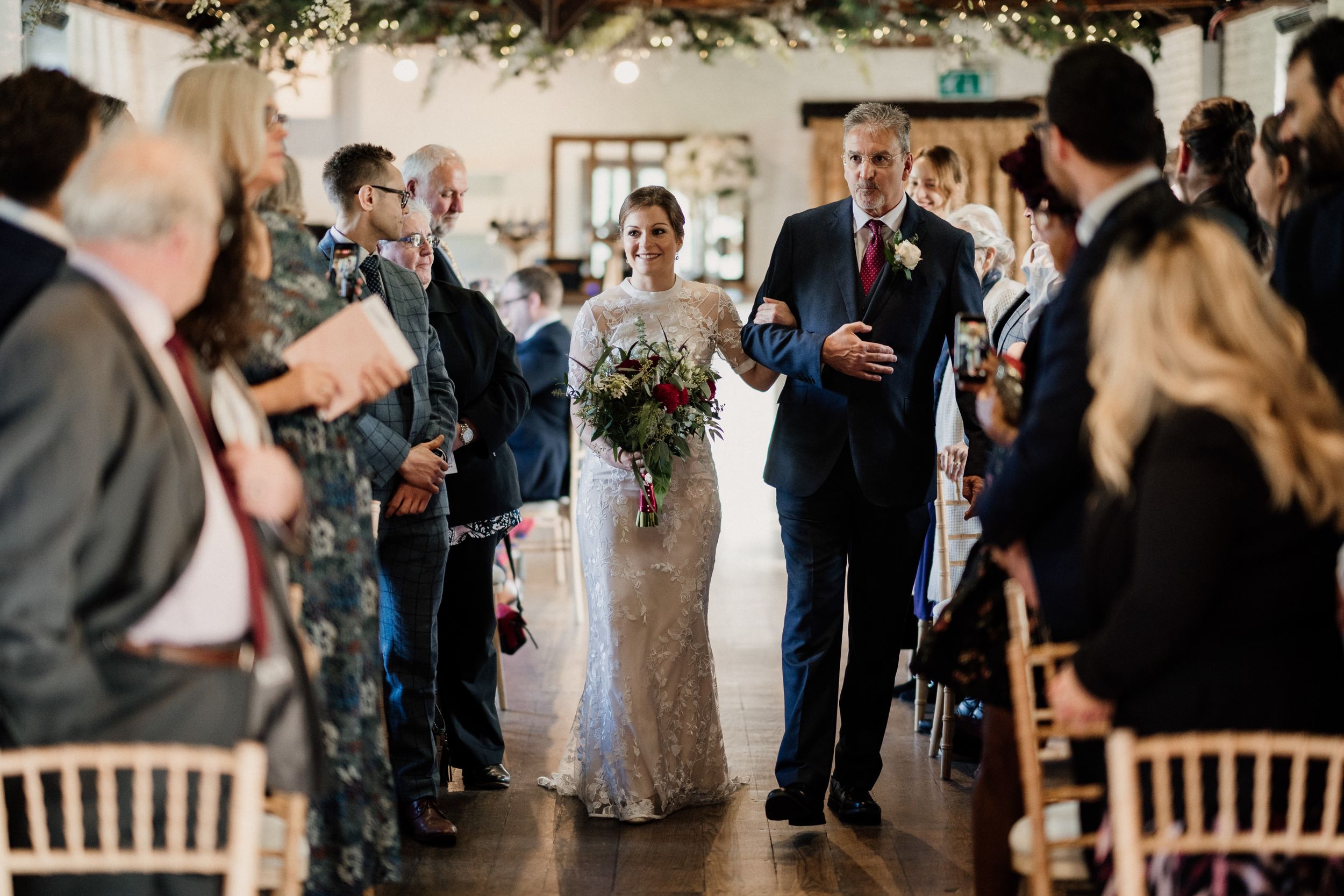 Indoor wedding ceremony with guests standing in aisle during processional.